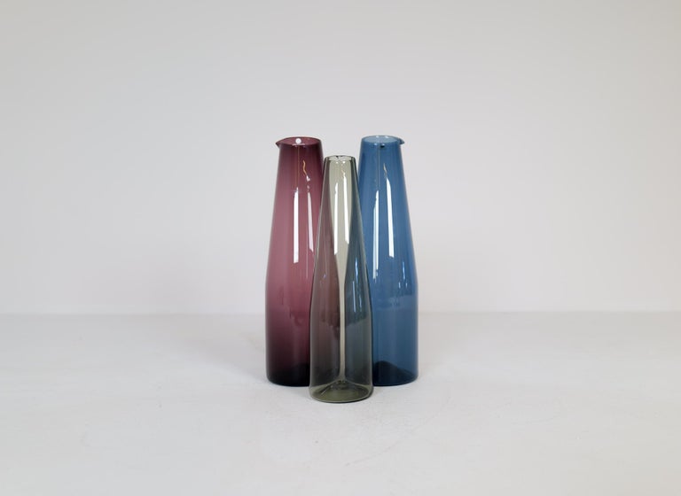 Nicely handcrafted art carafes produced by Iittala in 1956-1962 and designed by Timo Sarpaneva. Wonderful worked with a nice deep red and blue color with one smaller in grey / sand color. 

Very good vintage condition. 

Fully signed in the