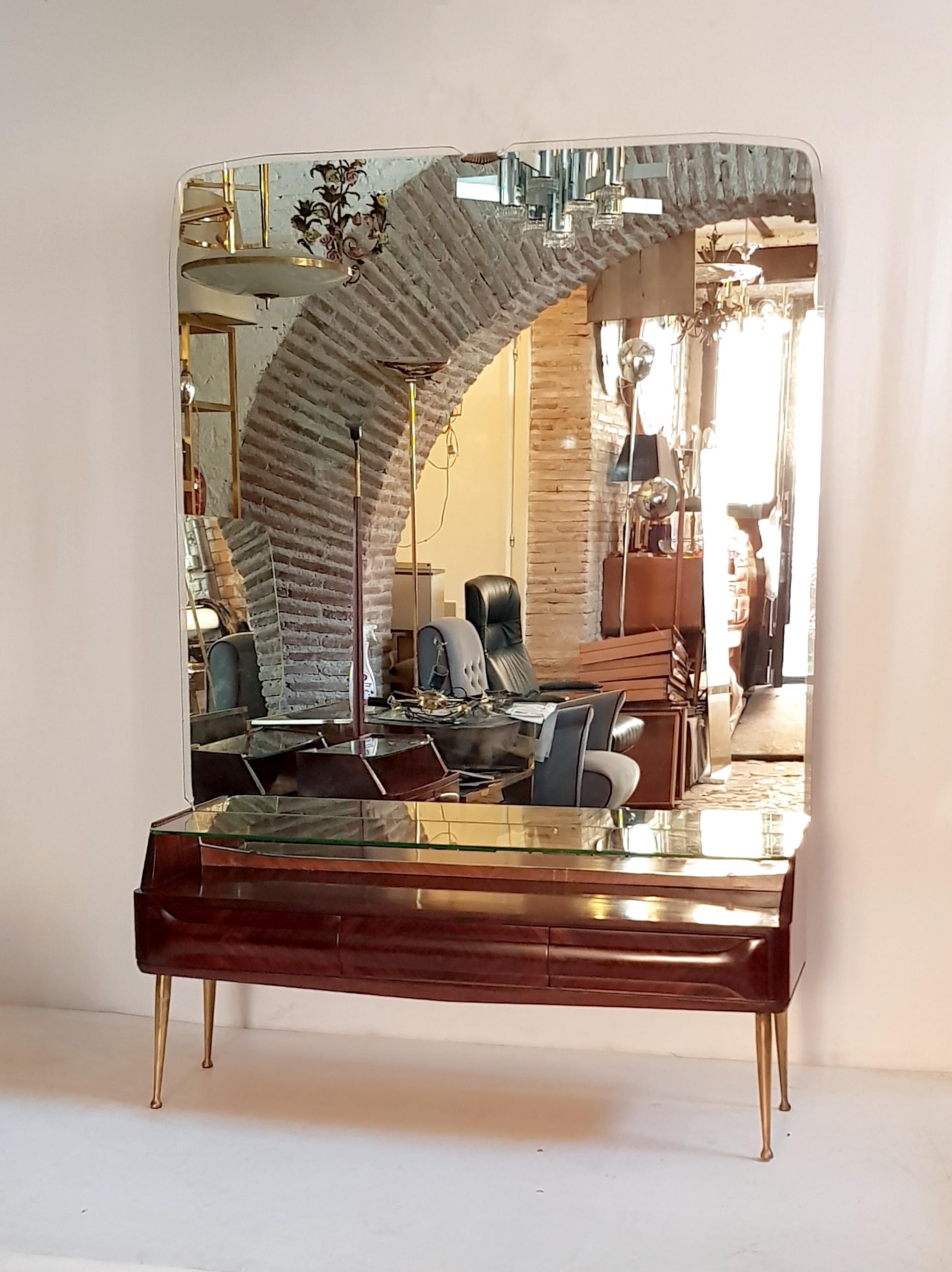 A console mirror table by Vittorio Dassi produced for his own company Dassi Lissone in jacaranda with spider legs in brass. It has three drawers and a shelf in clear glass which meets the mirror. The mirror has one small chip, see picture, but it