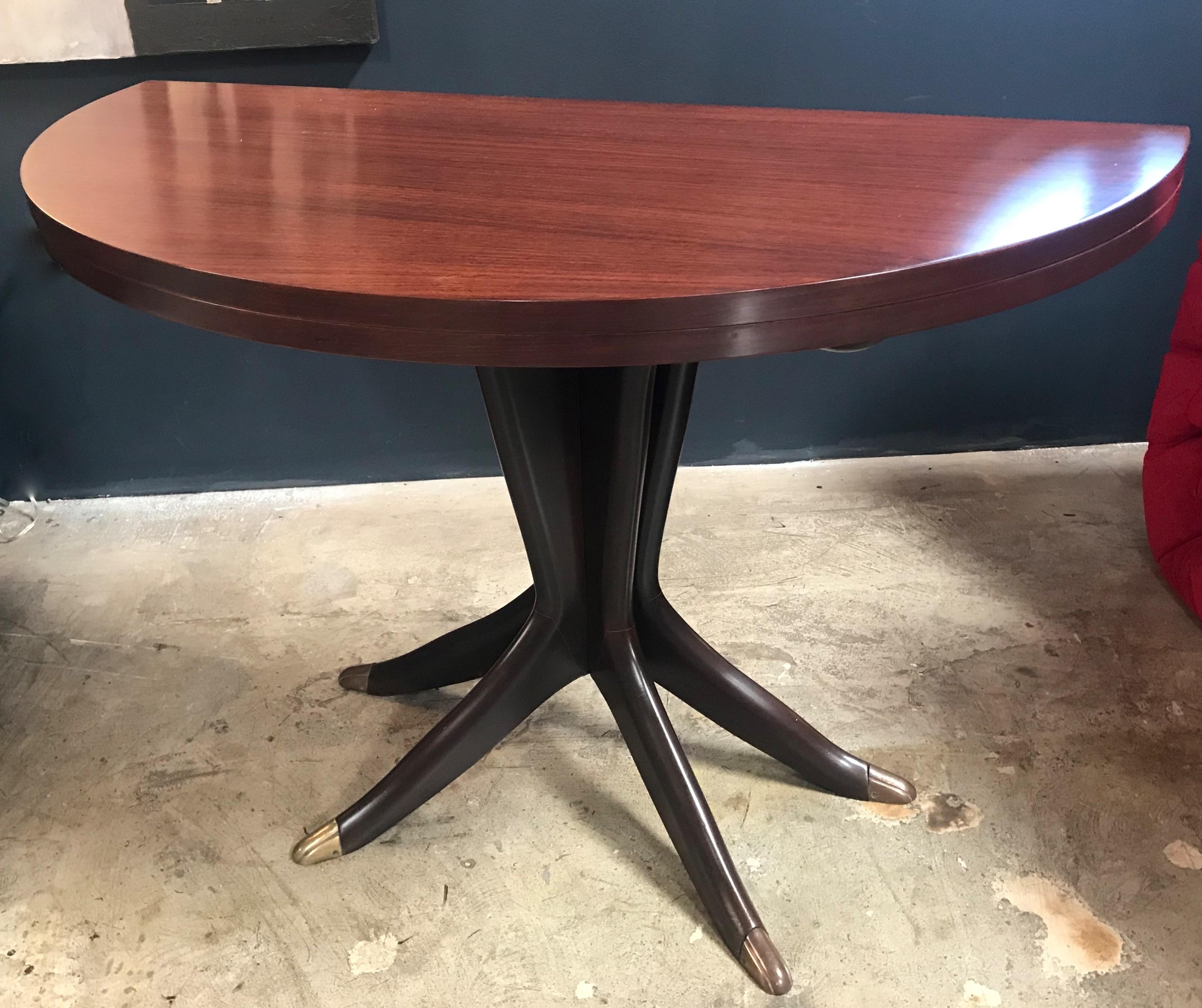 An Italian midcentury small sculptural console table on a sort of tripod with 4 wood legs leading and feet in brass suspending the small Rosewood console that becomes a nice round table (Diam. 40
