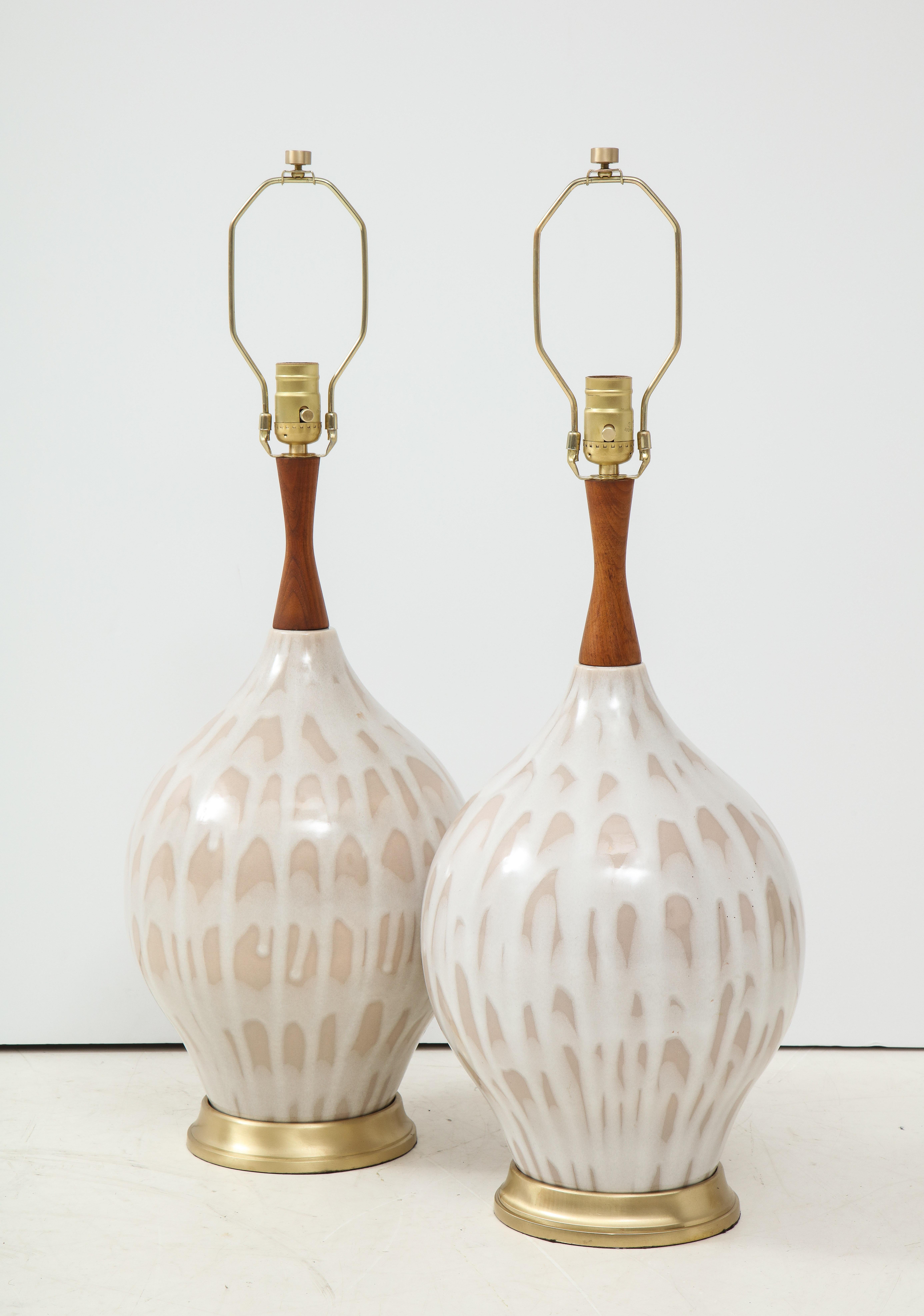Pair of midcentury ceramic lamps featuring a matte cream and taupe glaze and walnut spindle necks, on brushed brass bases. Rewired for use in the USA, 100W max.