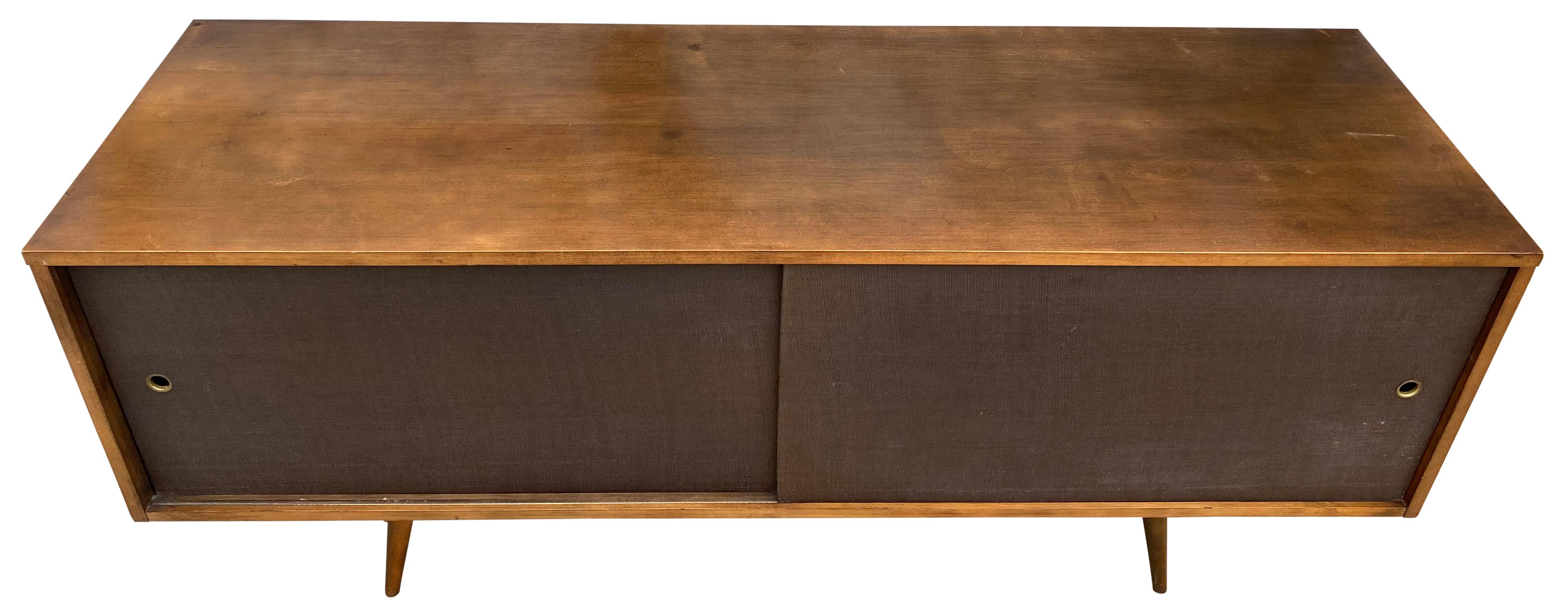 Beautiful midcentury low credenza by Paul McCobb circa 1950 planner group #1513 has 2 adjustable shelves with pins - solid maple construction has a Beautiful Walnut finish. All original brown cloth sliding front doors with brass finger pull sits on