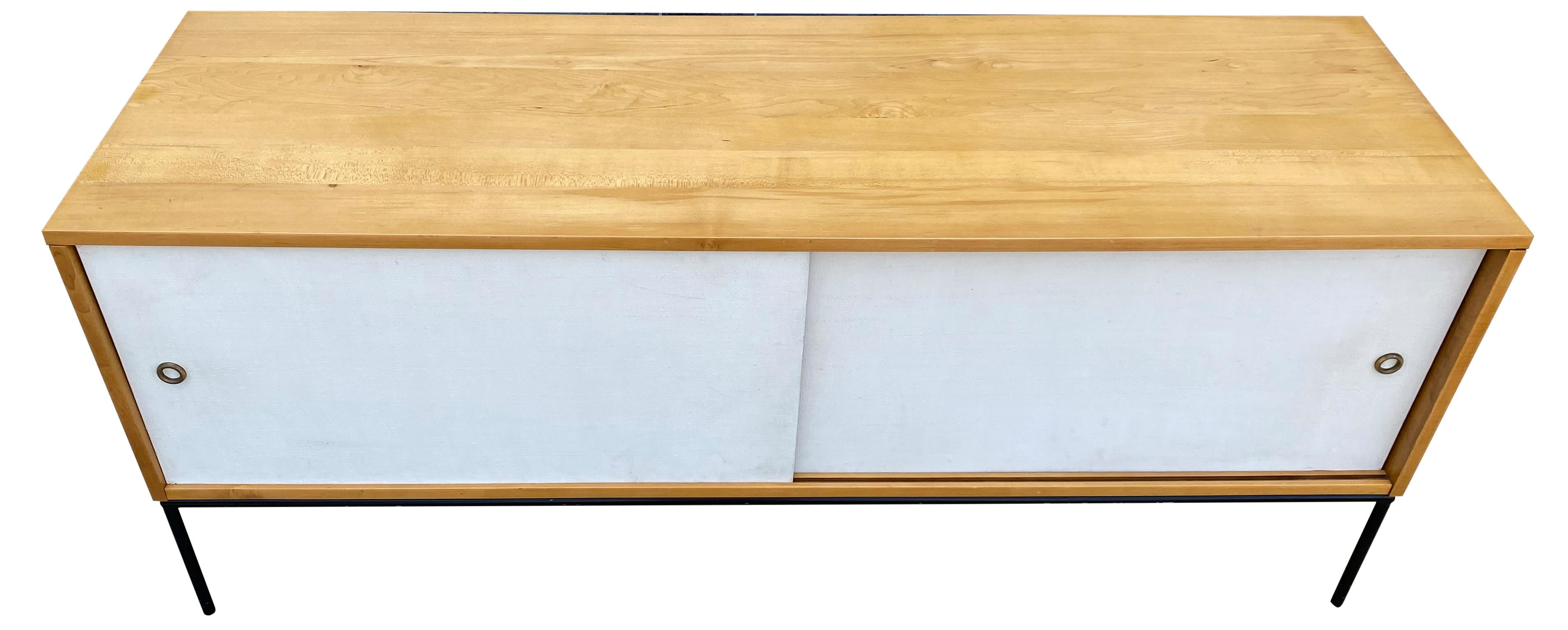 Beautiful midcentury low credenza by Paul McCobb circa 1950 planner group #1513 has 2 adjustable shelves with pins - solid maple construction has a Beautiful Blonde finish. All original white cloth sliding front doors with brass finger pull sits on