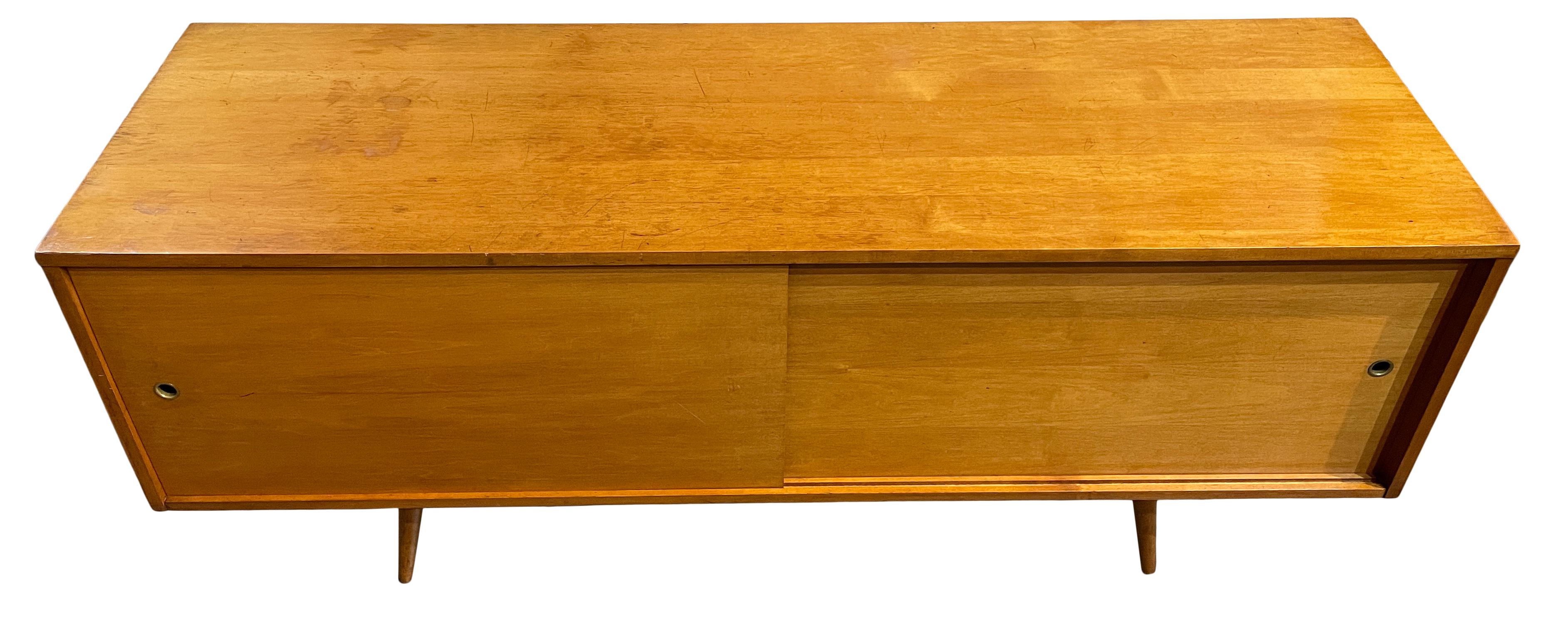 Beautiful midcentury low credenza cabinet with sliding doors by Paul McCobb circa 1950 planner group #1513 - solid maple construction has a Blonde maple finish. All original Wood sliding front doors with brass finger hole pull sits on 4 tapered
