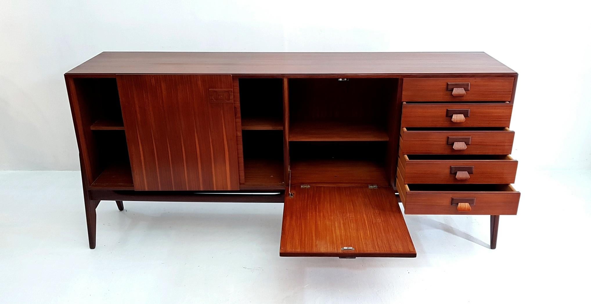 This credenza in teak was made by Frattelli (brothers) Proserpio in the 1960s in the factory that is running to this day. The credenza is resting on a stand without any screws or attachments and is yet stabile. There are two sliding doors, a dry bar