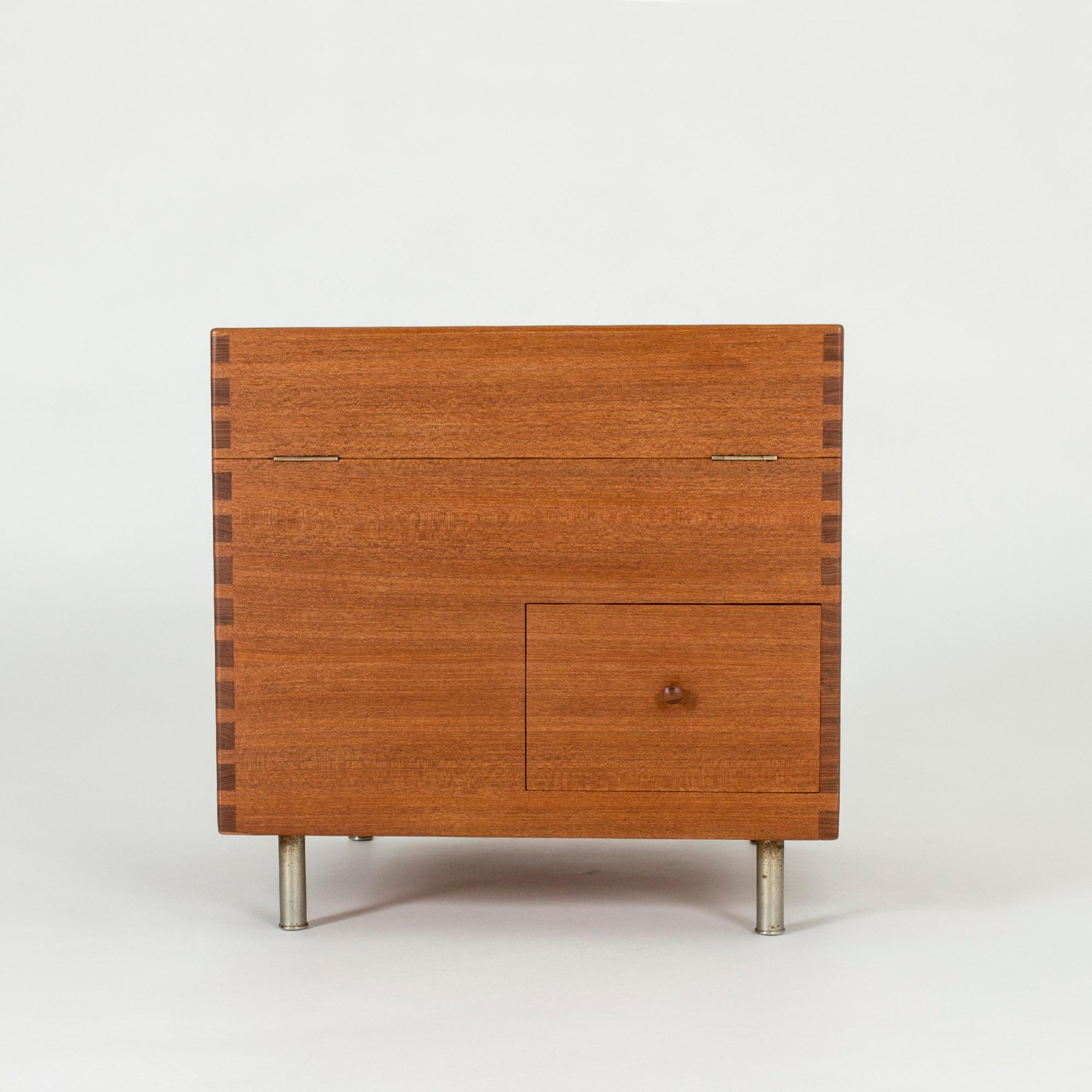 Rare cubical bar cabinet, model “8034”, designed by Hans J. Wegner in 1956. Made in teak with a decorative pattern created at the joinery of the sides. Has one drawer and two compartments inside. Steel legs.