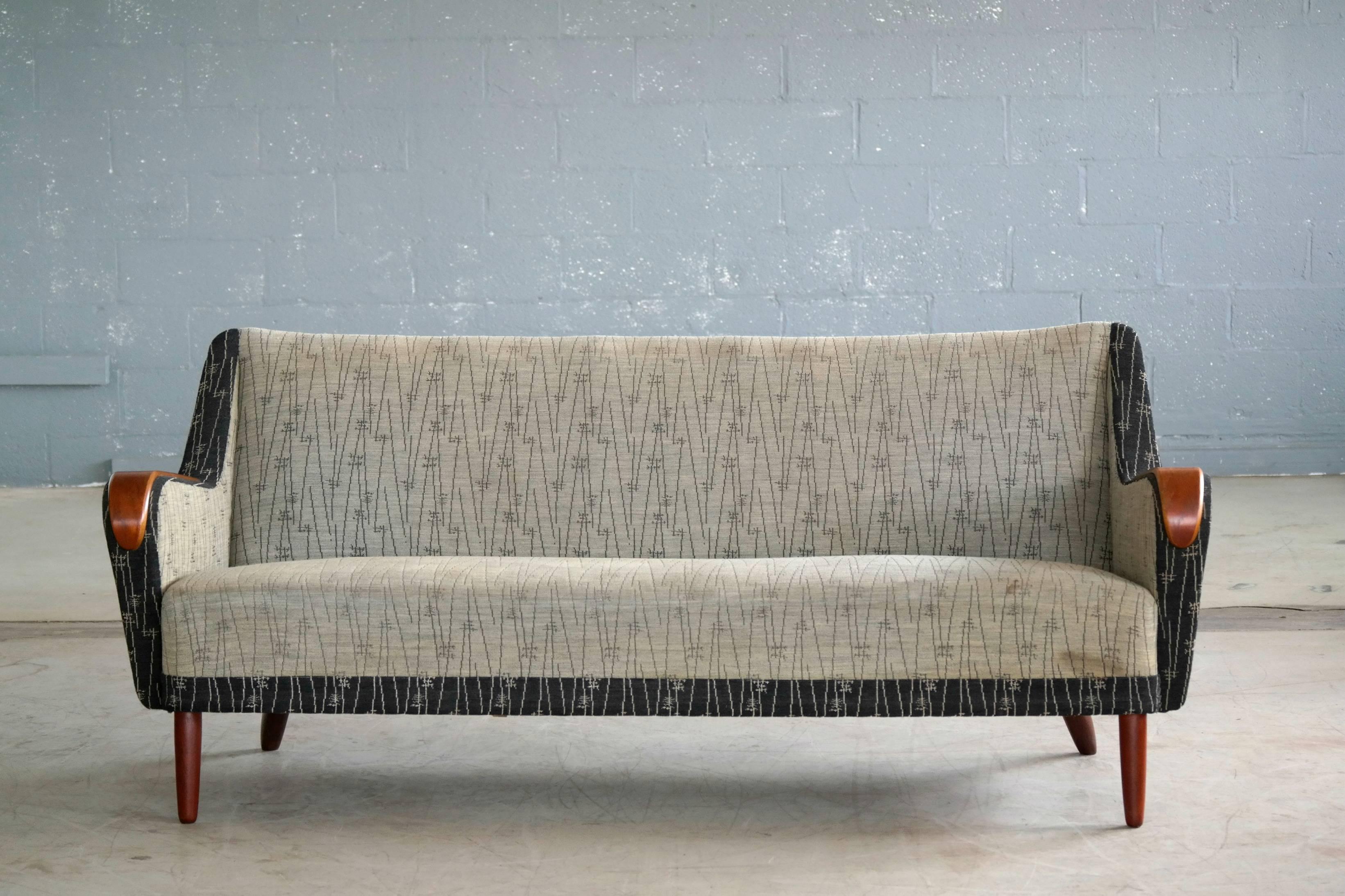 Very Classic and ultra cool Danish three-seat sofa epitomizing the 1950s and reminiscent of Kurt Olsen's design style. Built on a sturdy beech wood frame and raised on solid teak legs with teak accents on the armrests. We love the stance of this