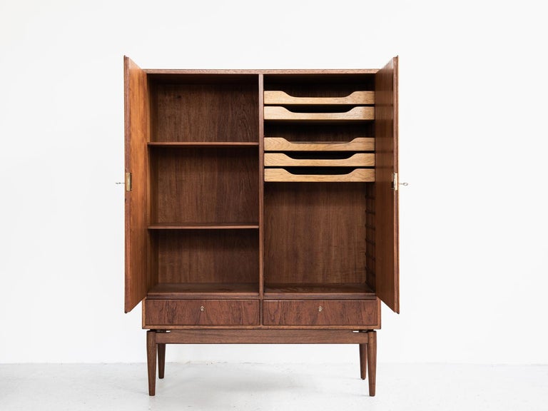 Midcentury cabinet made in Denmark in the 1960s. This well designed higher cabinet has 2 doors and 2 drawers. Inside there are 2 shelves and 5 drawers. All parts are a proof of good quality manufacturing. The doors have beautiful drawings in the