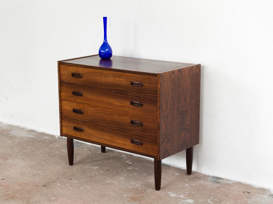 This midcentury chest of four drawers in rosewood is manufactured in Denmark in the 1960s. Good quality manufacturing with typical shape of drawer handles and a nice color play in the wood on the front; and beautiful drawings in the wood on sides