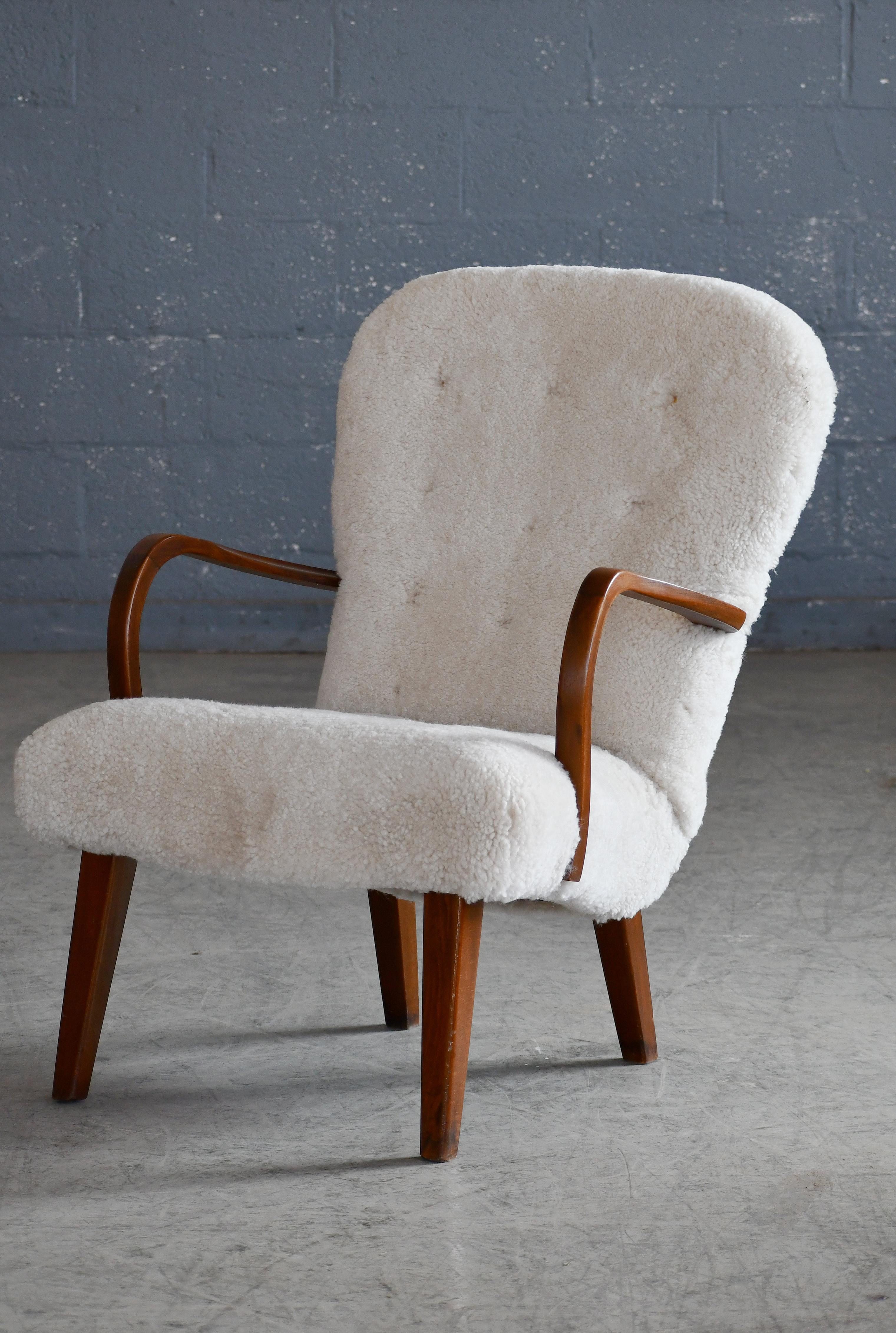 Charming clam-style lounge chair made in Denmark from stained and varnished beech wood. Recovered in luxurious putty colored curly textured sheepskin from Garrett Leather. The design bears resemblance to the famous model Pragh by Designer team