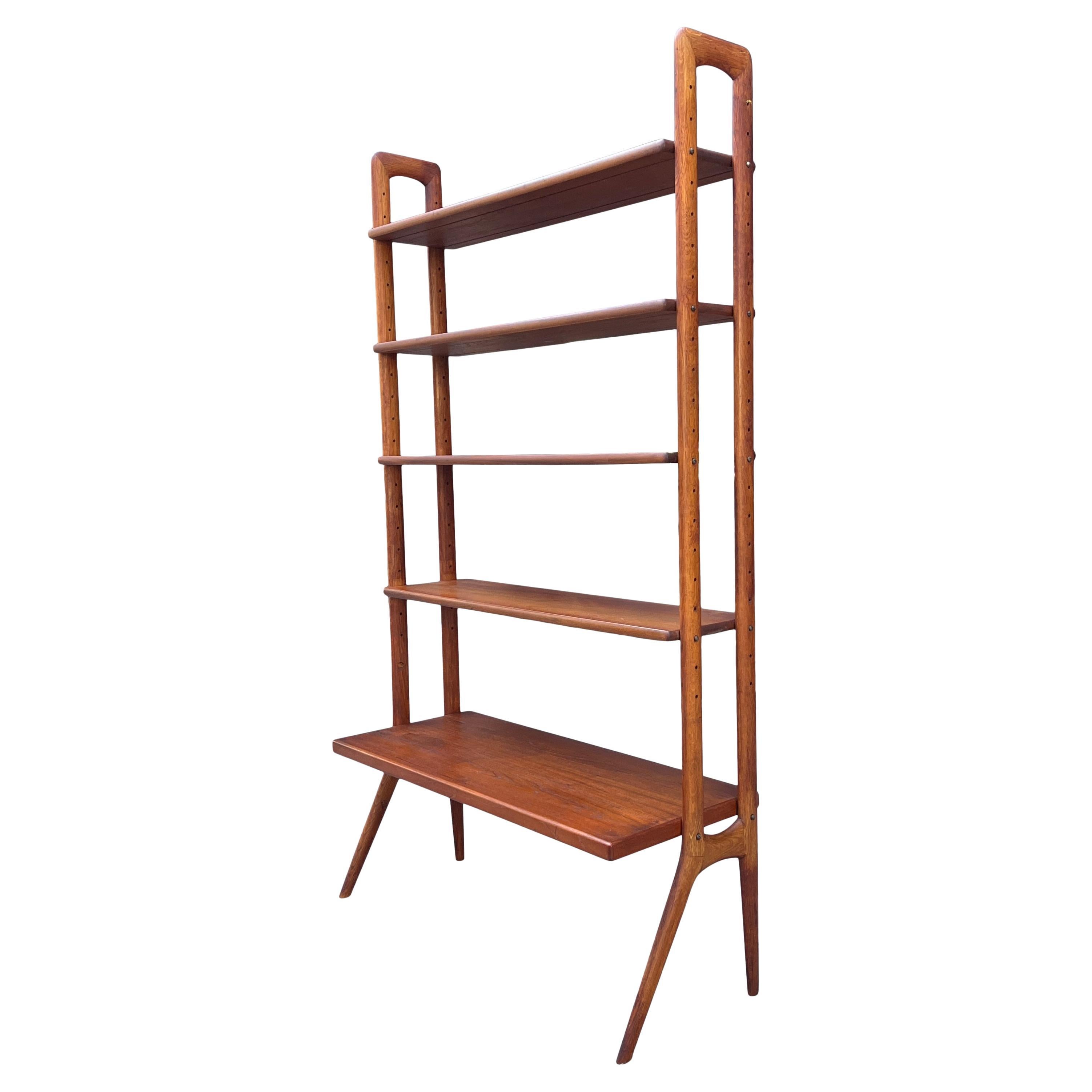 Danish teak wood free standing bookshelf or wall unit designed by Kurt Ostervig crafted by Povl Dinesen. Five shelves (4 shelves are 10'' lower shelf is deeper at 16''). The shelves are adjustable, and the holes for repositioning form an integral