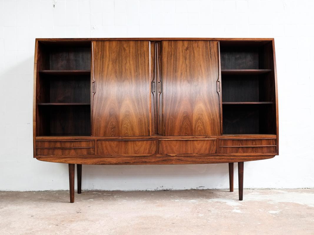 Midcentury highboard made in Denmark in the 1960s. A true top quality piece with a nicely curved front, including the doors. Inside there is a very detailed bar closet in the middle compartment with light behind the glass. This highboard is