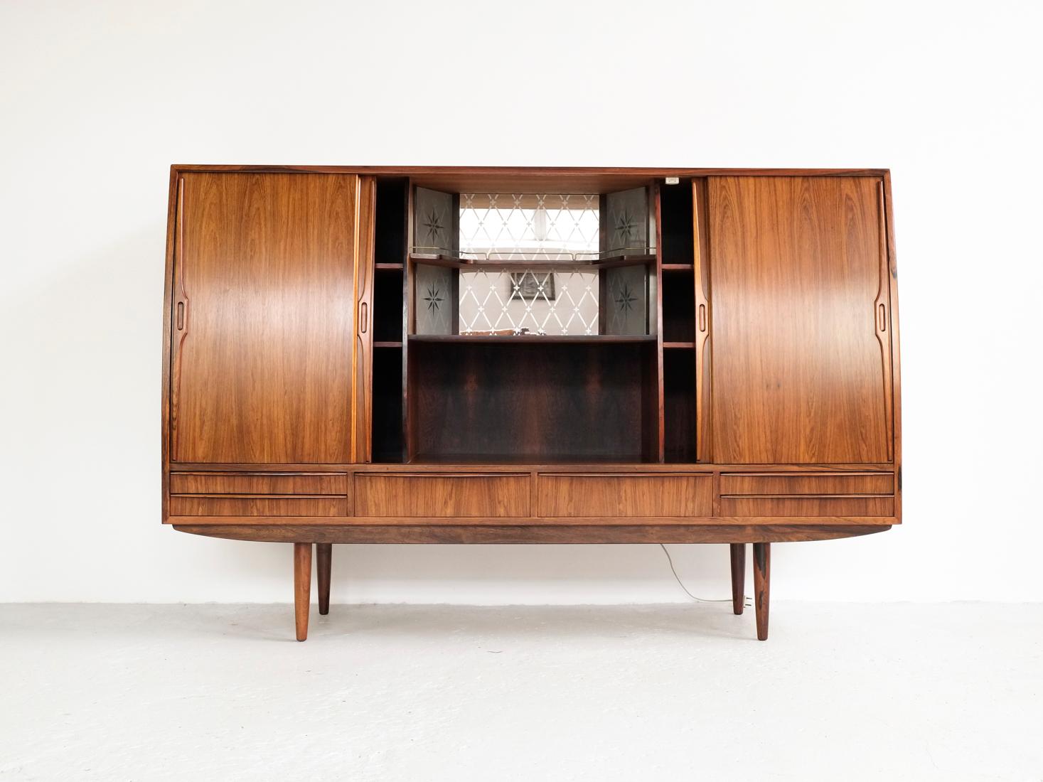Midcentury highboard in rosewood made in Denmark in the 1960s. A true top quality piece with a nicely curved front, including the doors. Inside there is a very detailed bar closet in the middle compartment with light behind the glass. This highboard
