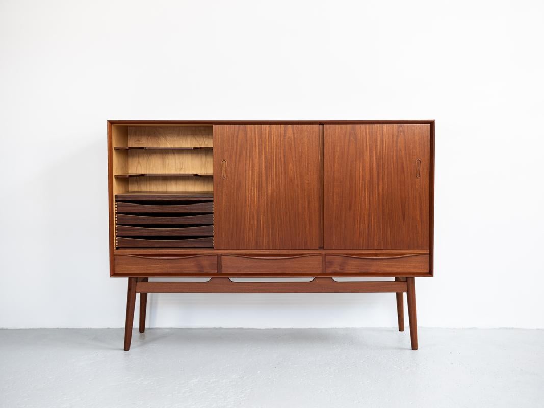 Midcentury highboard made in Denmark in the 1960s. This well designed high sideboard has 3 sliding doors and 3 drawers. Inside there is a practical bar compartment on the left side. This highboard is in teak and in perfect condition.