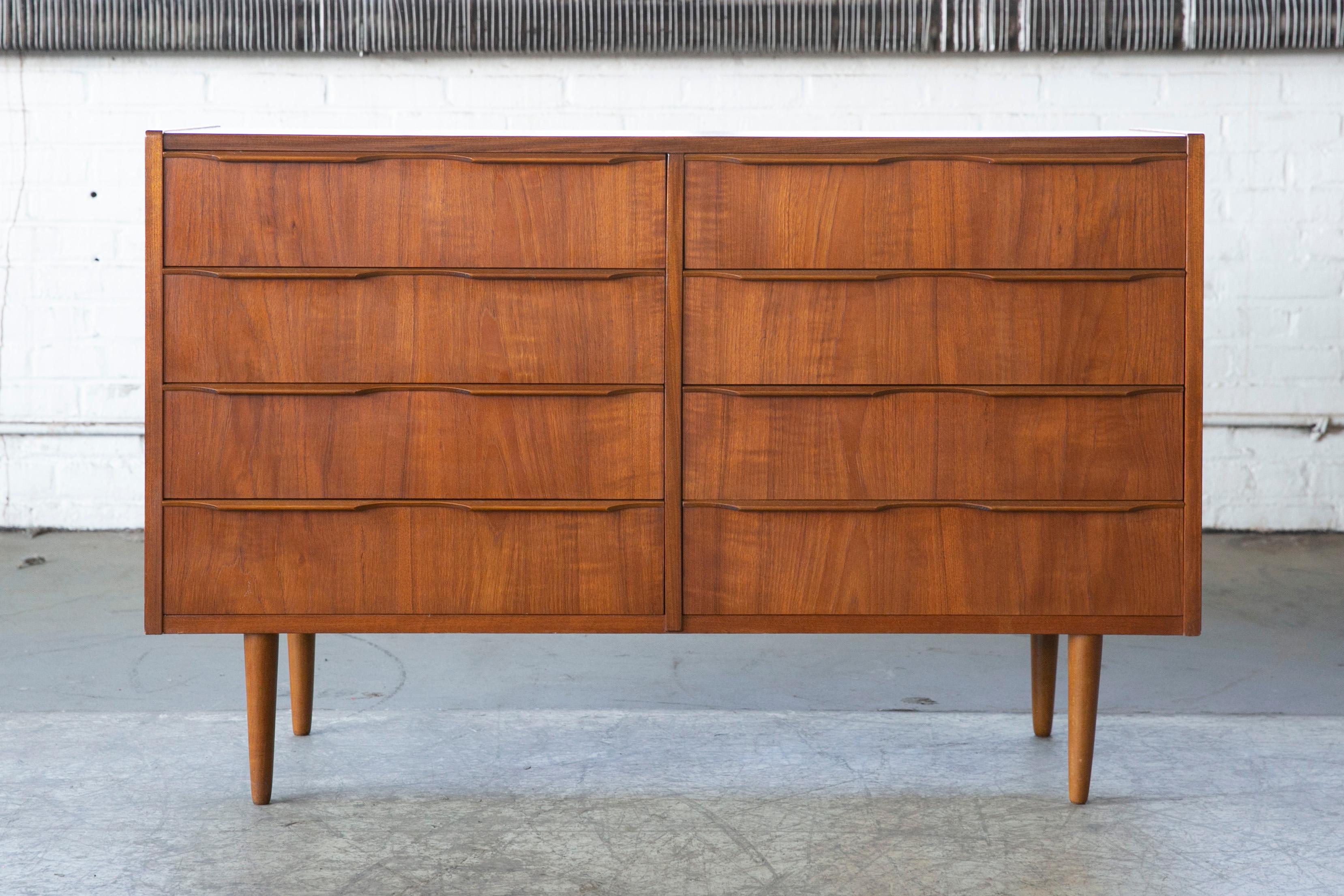 Rare to find 1960s Danish modern teak double dresser. Nice bookmatched wood grain. Drawers are constructed with dovetail joinery and are complimented by the finely carved hand pulls giving this simple dresser an elegant touch. Tapered teak wood legs