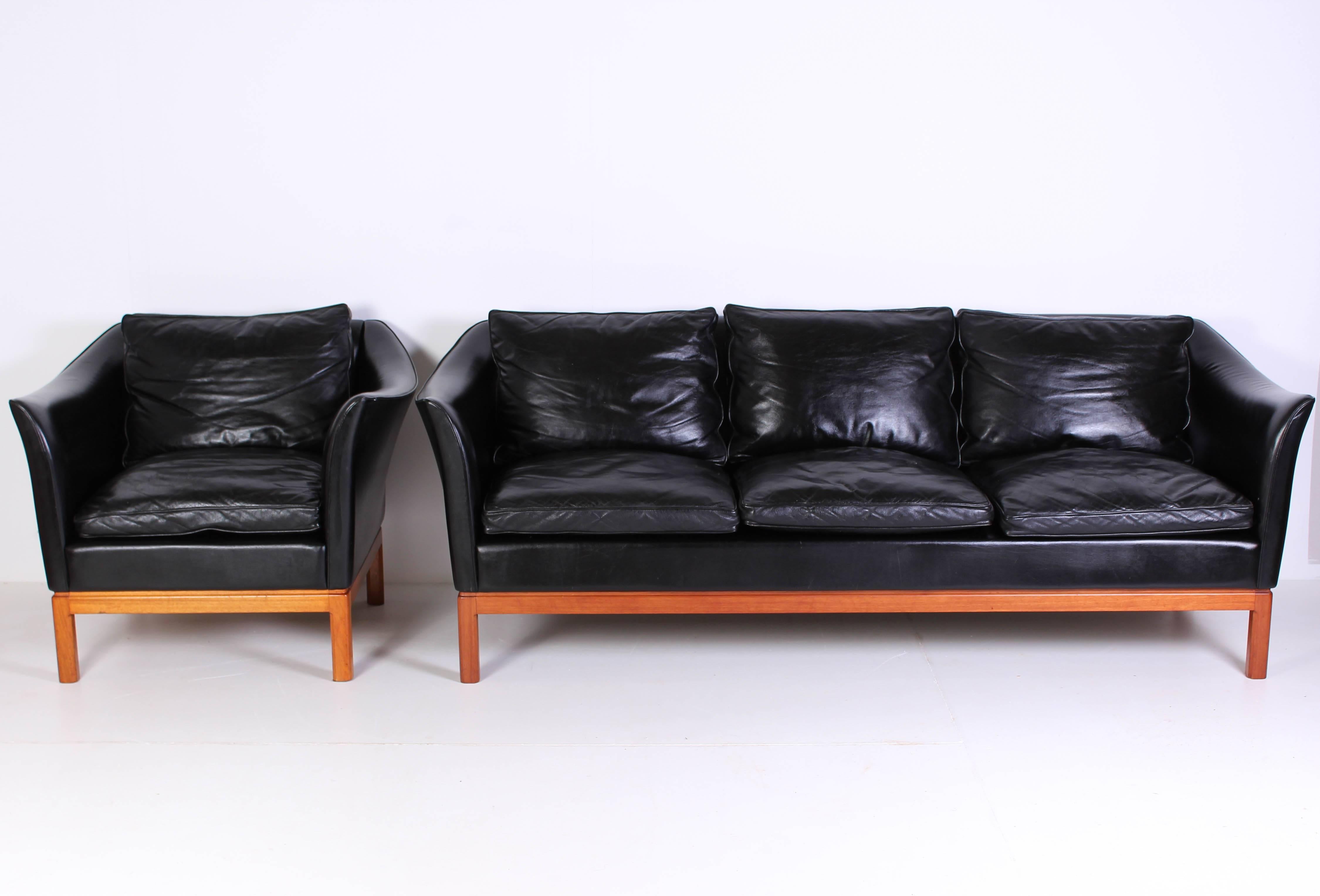 Set of midcentury three seat sofa and lounge chair with original black leather upholstery. The set is from circa 1960 and originates from Denmark. The curved armrests is a very nice detail that really makes the set stand out. The legs are made out