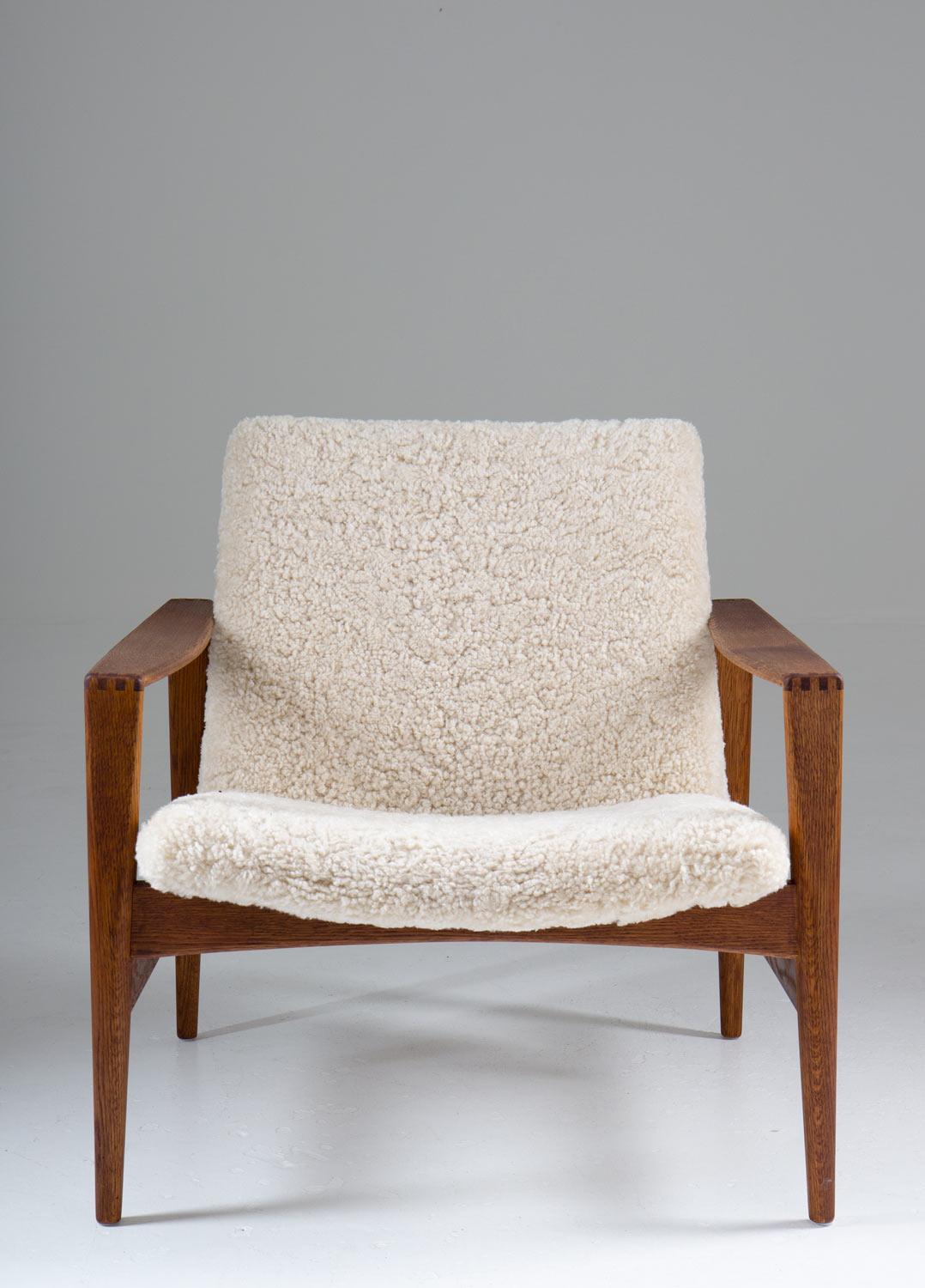 Pair of rare Mid-Century Modern lounge chair by Niels Kofoed for Niels Eilersen, 1960s. 

These chairs have a distinct design with beautiful details. They feature a stained oak frame, holding the seating and backrest, upholstered in off-white