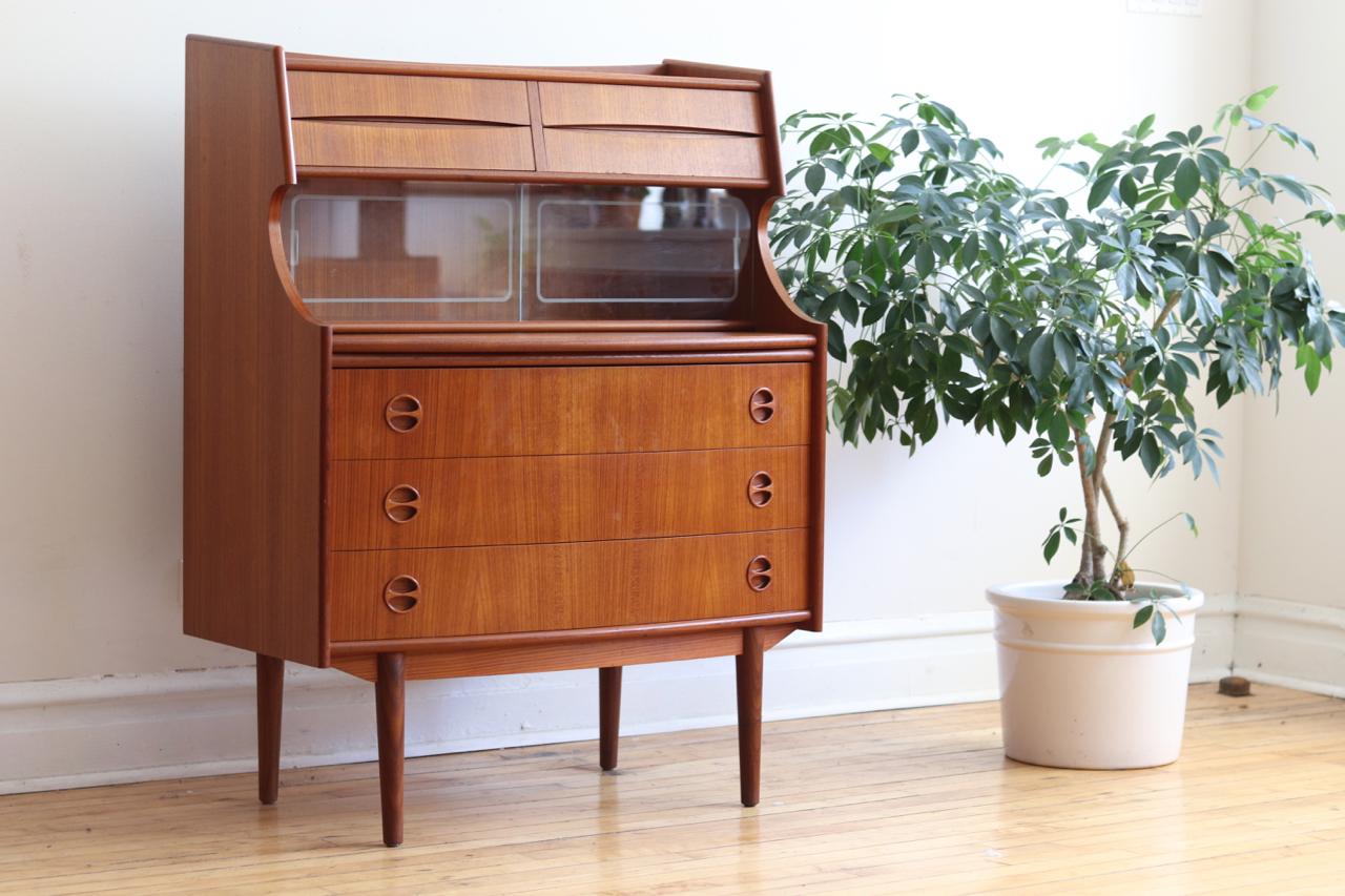 Danish Mid-Century Modern teakwood secretary desk.
Just imported from Denmark!
Designed by Arne Vodder for Sibast Mobler.
Hidden shelf extends to create a desktop surface.
Etched glass sliding panels.
Four small drawers on top and 3 large