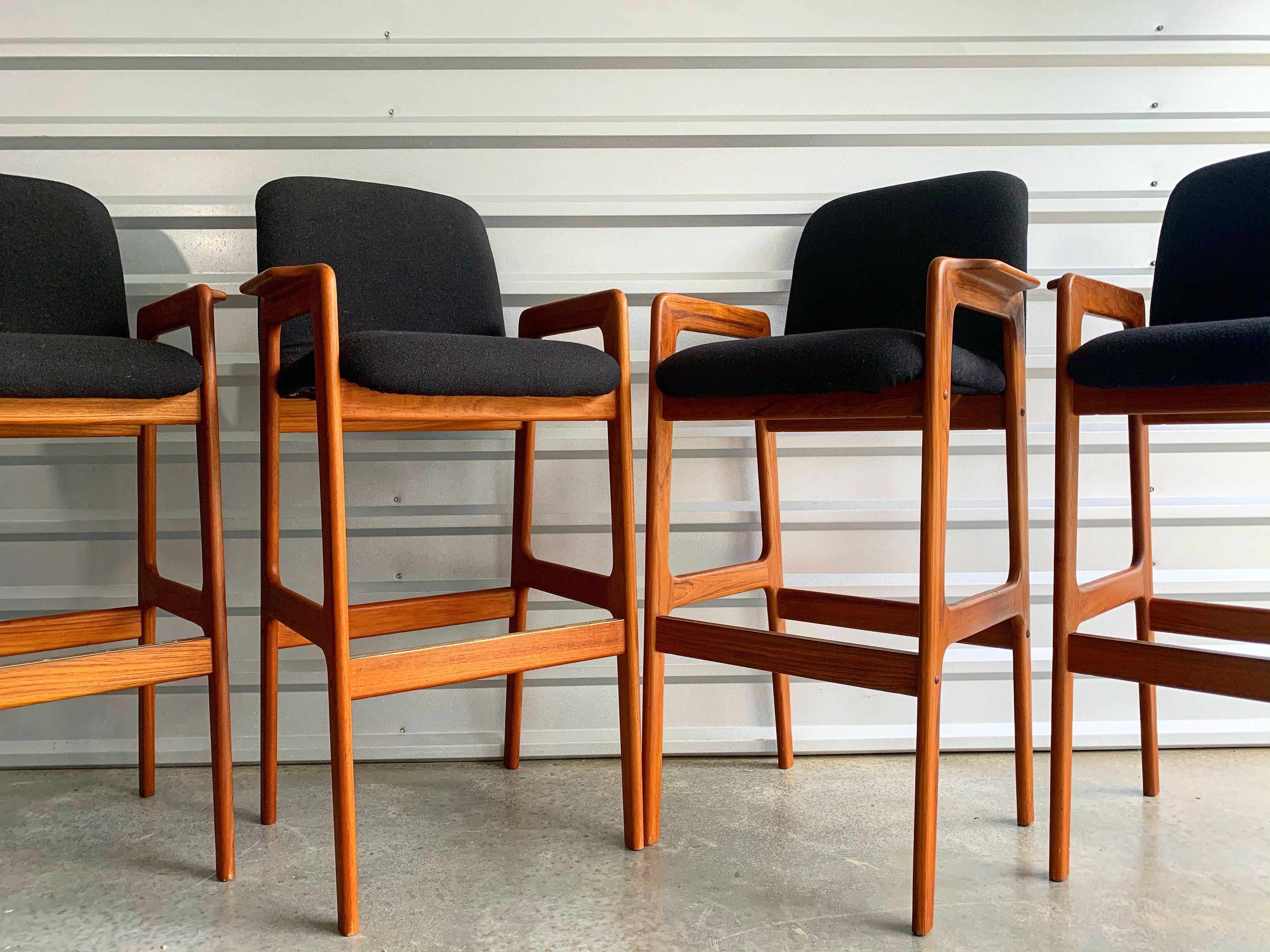 Set of 4 midcentury Danish modern solid teak bar height bar stools by Benny Linden. Original black wool tweed upholstery and corrugated brass plate on the footrest.
Teak frames are clean, sound and sturdy with a rich amber hue. Original black
