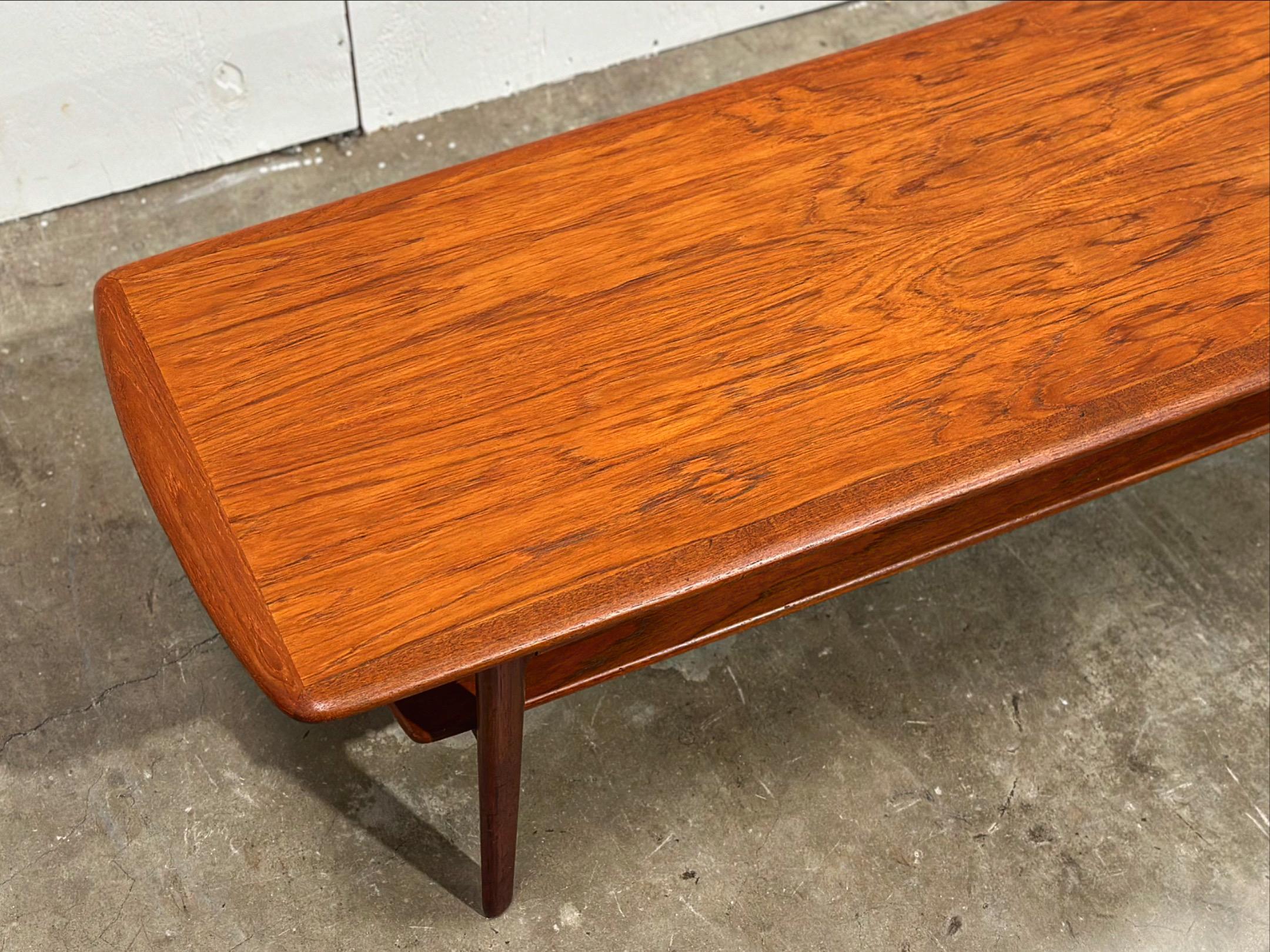 Mid century Danish modern teak cocktail or coffee table designed by Svend Age Madsen for Karl Lindegaard. Long rectangular top with rounded edges and a convenient lower shelf. Solid sculpted old growth teak legs.
Fully restored by our team - this