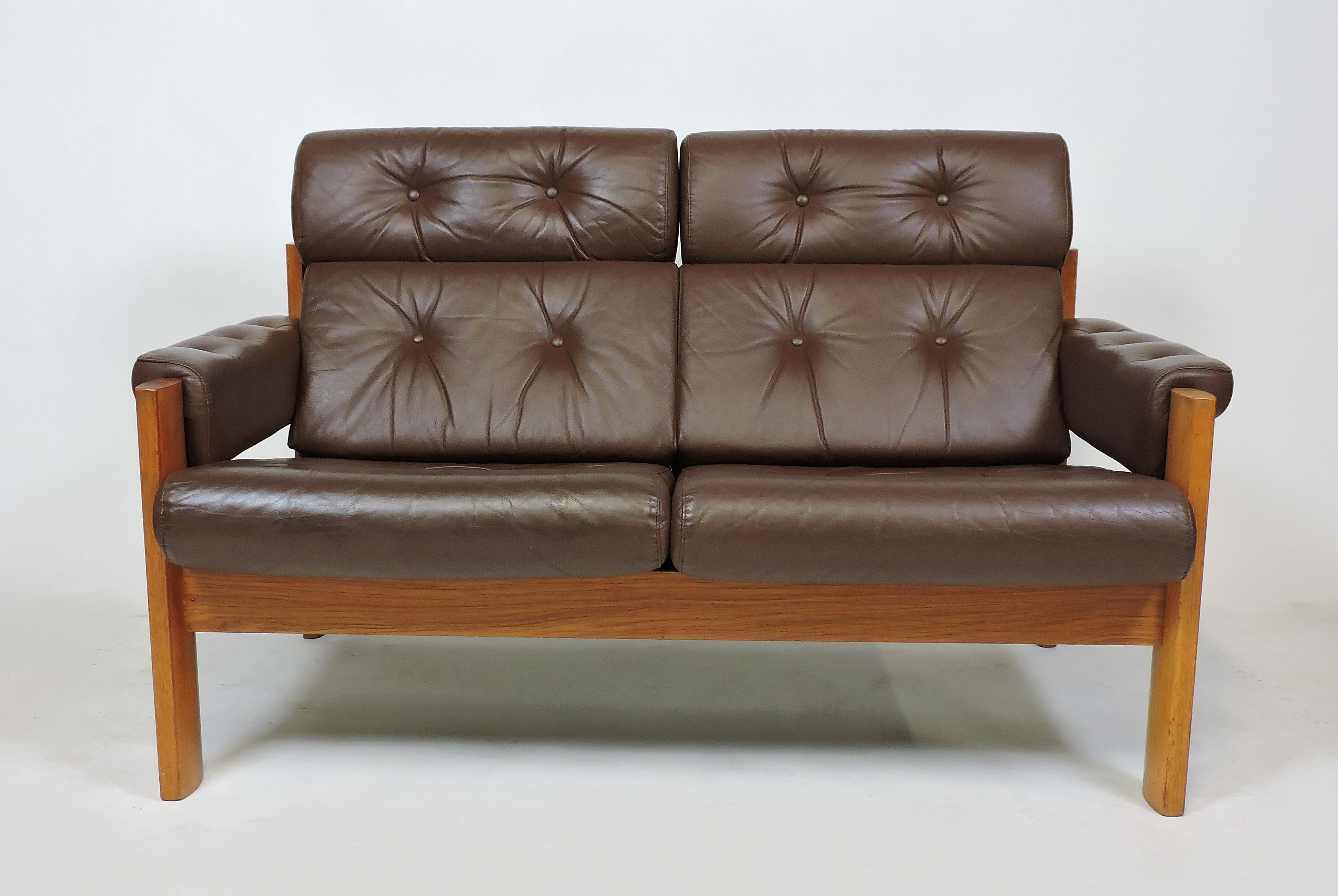 Handsome and comfortable amigo two-seat sofa made in Norway by high quality furniture manufacturer, Ekorness. It has great craftsmanship with a sculpted solid teak frame and dark brown tufted leather upholstery. All of the cushions are removable and