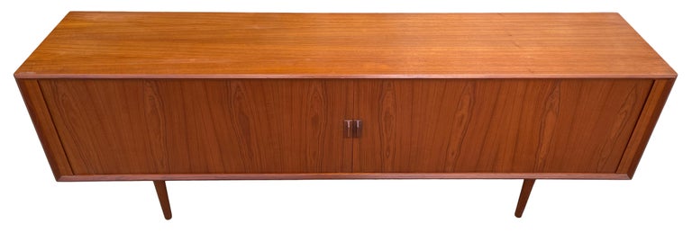 Stunning long mid-century Danish modern teak credenza sideboard. Beautiful tambour doors reveal (1) adjustable shelf. Solid teak legs and pulls. In excellent vintage condition. Beautiful credenza with lots of room for storage/records. Very heavy