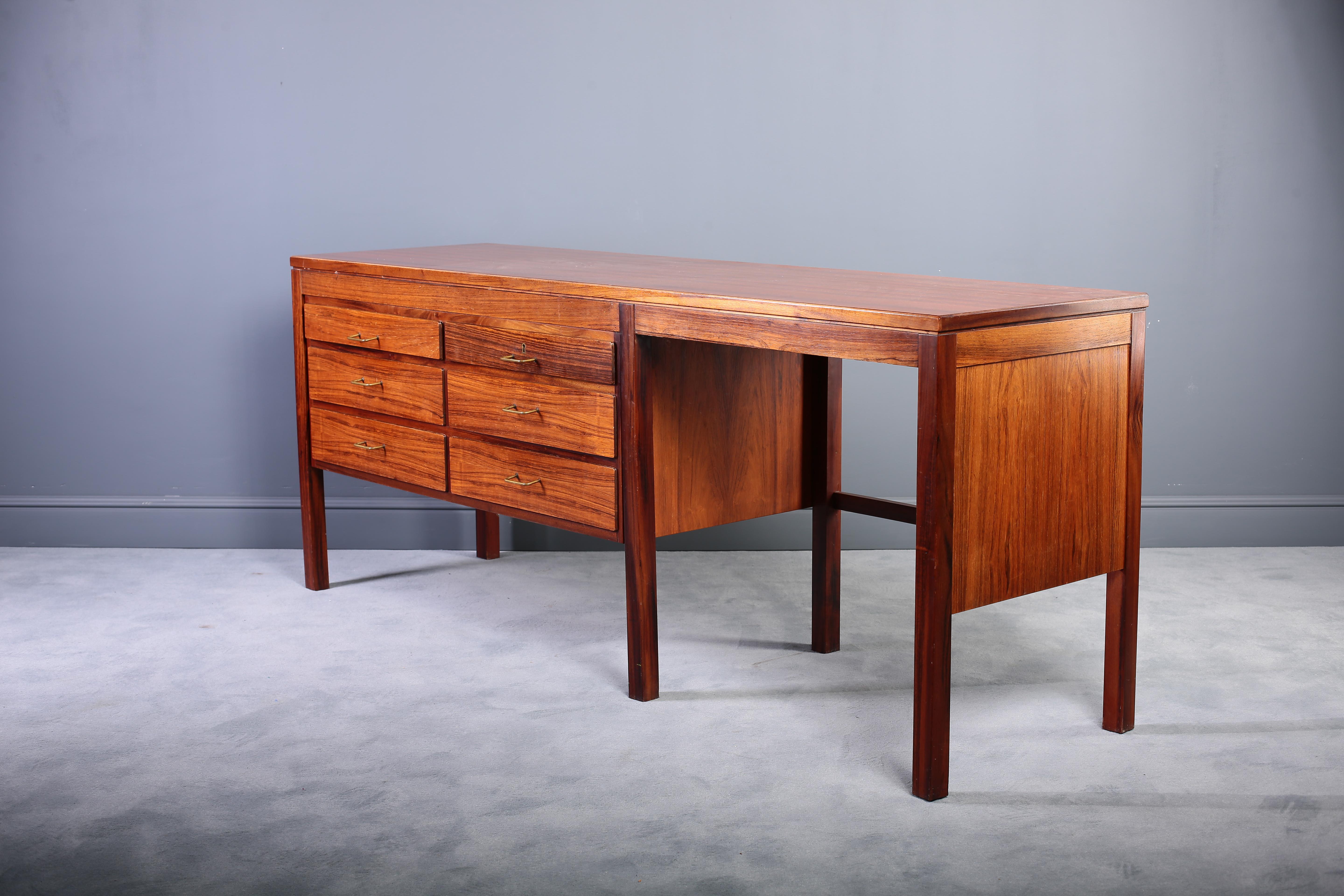 This Danish modern dresser or desk is crafted in Brazilian rosewood and provides six large drawers for storage. Each drawer is adorned with the original brass pull. It has an open work surface with wide leg space on the right of this piece. It is in