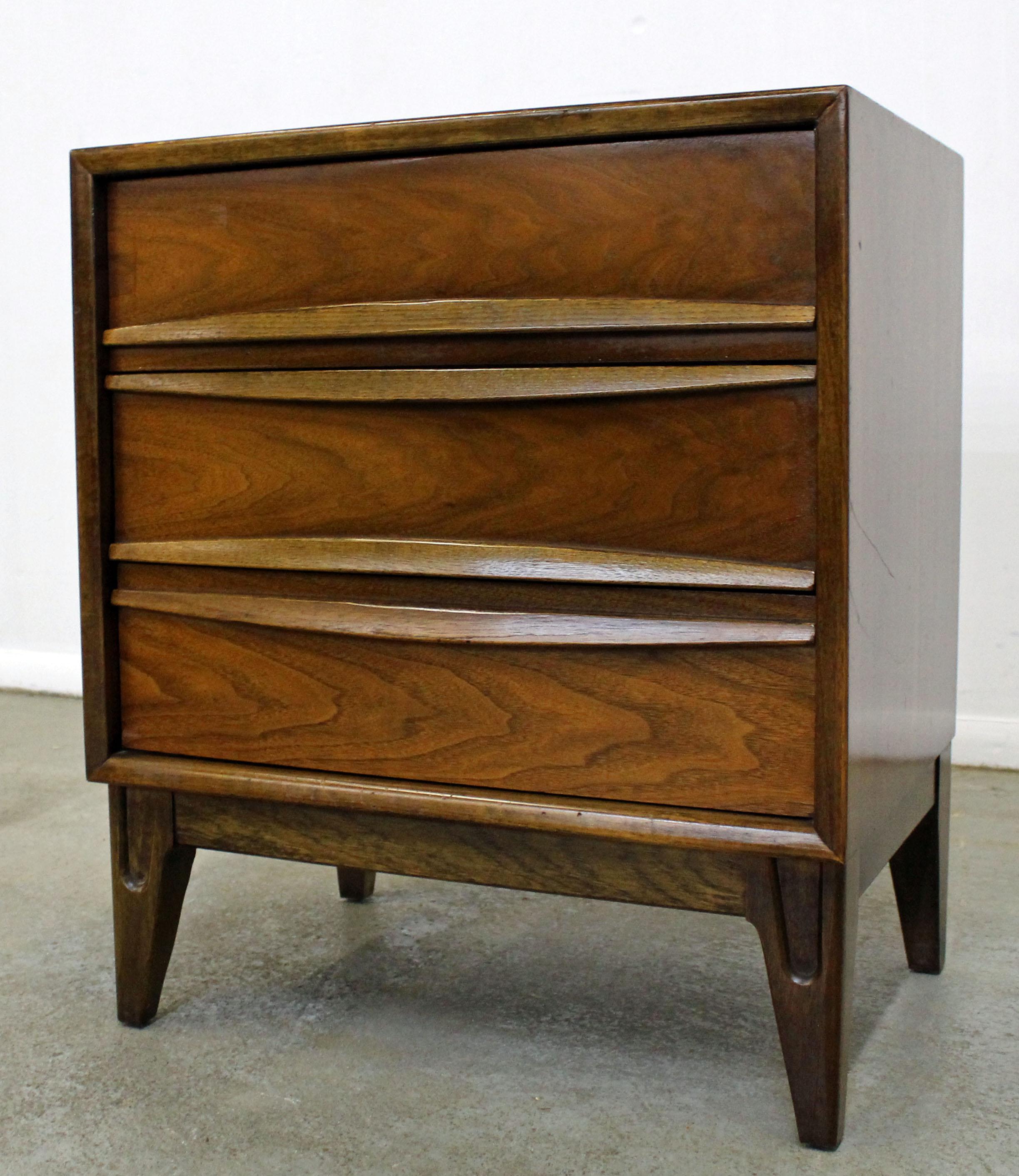 Offered is an excellent example of American Mid-Century Modern design. This is a single walnut nightstand with tapered legs, three dovetailed drawers, and sculpted pulls. It is in good condition, showing some age wear. It is not signed. Check out