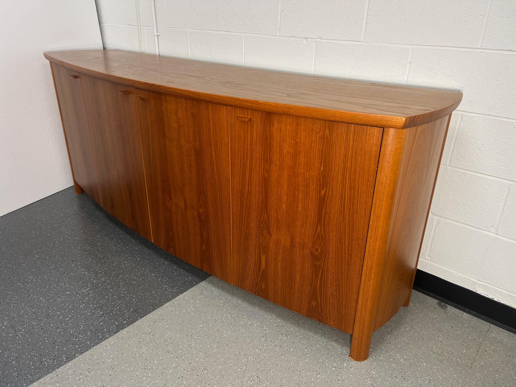 Outstanding teak veneer credenza or buffet by Skovby. Bow front design. Original label at the back. Lots of storage. Adjustable shelves. Fantastic condition. Small gouge on the left and small stain on the top. A little chipping at the bottom of the