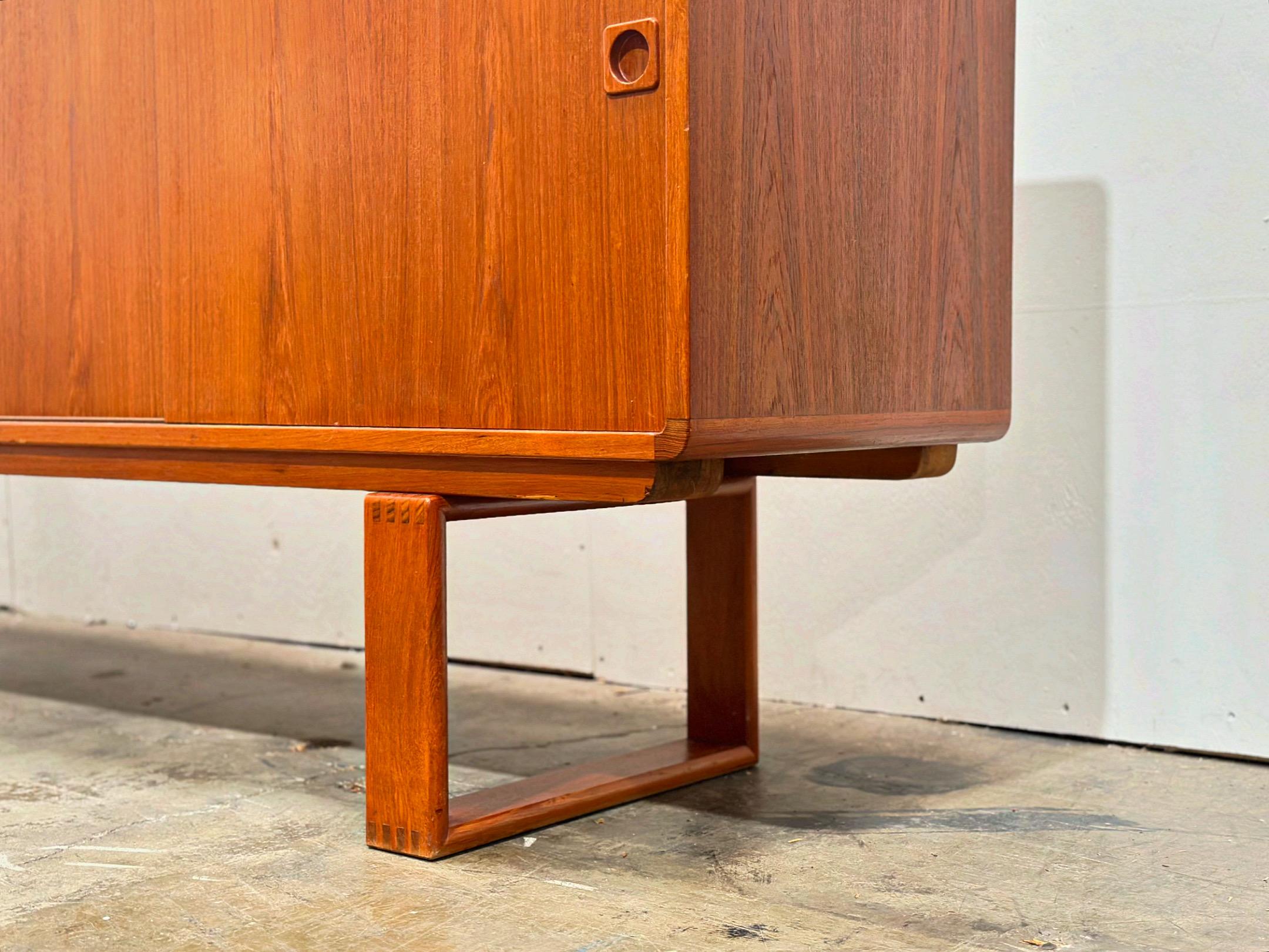 Long Danish modern sliding door credenza sideboard, circa 1970s. Sled style base with exposed dovetail joinery. Gorgeous from any angle. Four felt lined drawers on the left side with adjustable height shelving on the right. Excellent original