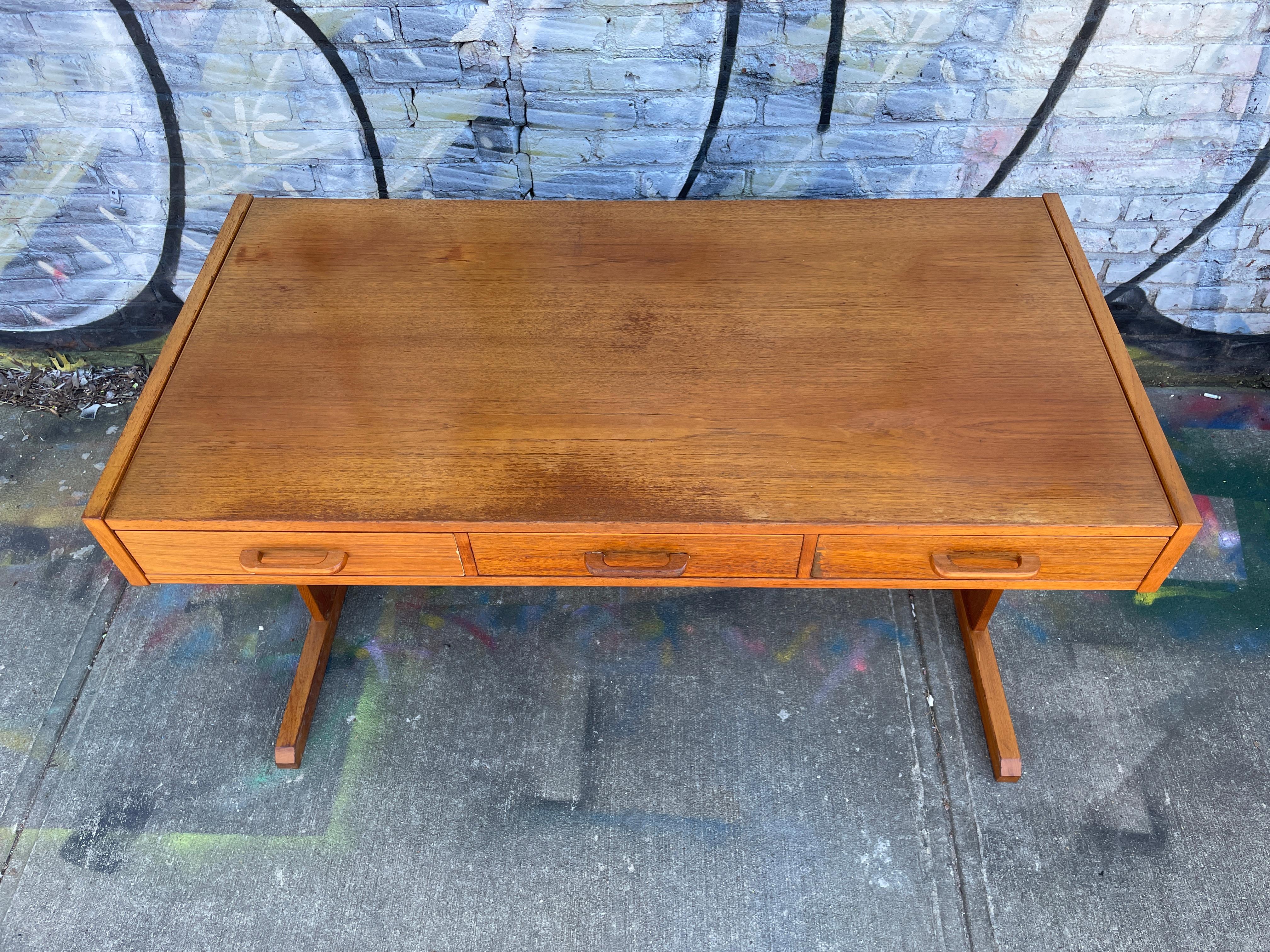 Danish modern teak desk with three drawers that have teak handles and a rectangular base. The drawers easily slide and are clean. original vintage condition and ready for use. Shows signs of use and patina. Desk top slides forward to reveal a hidden