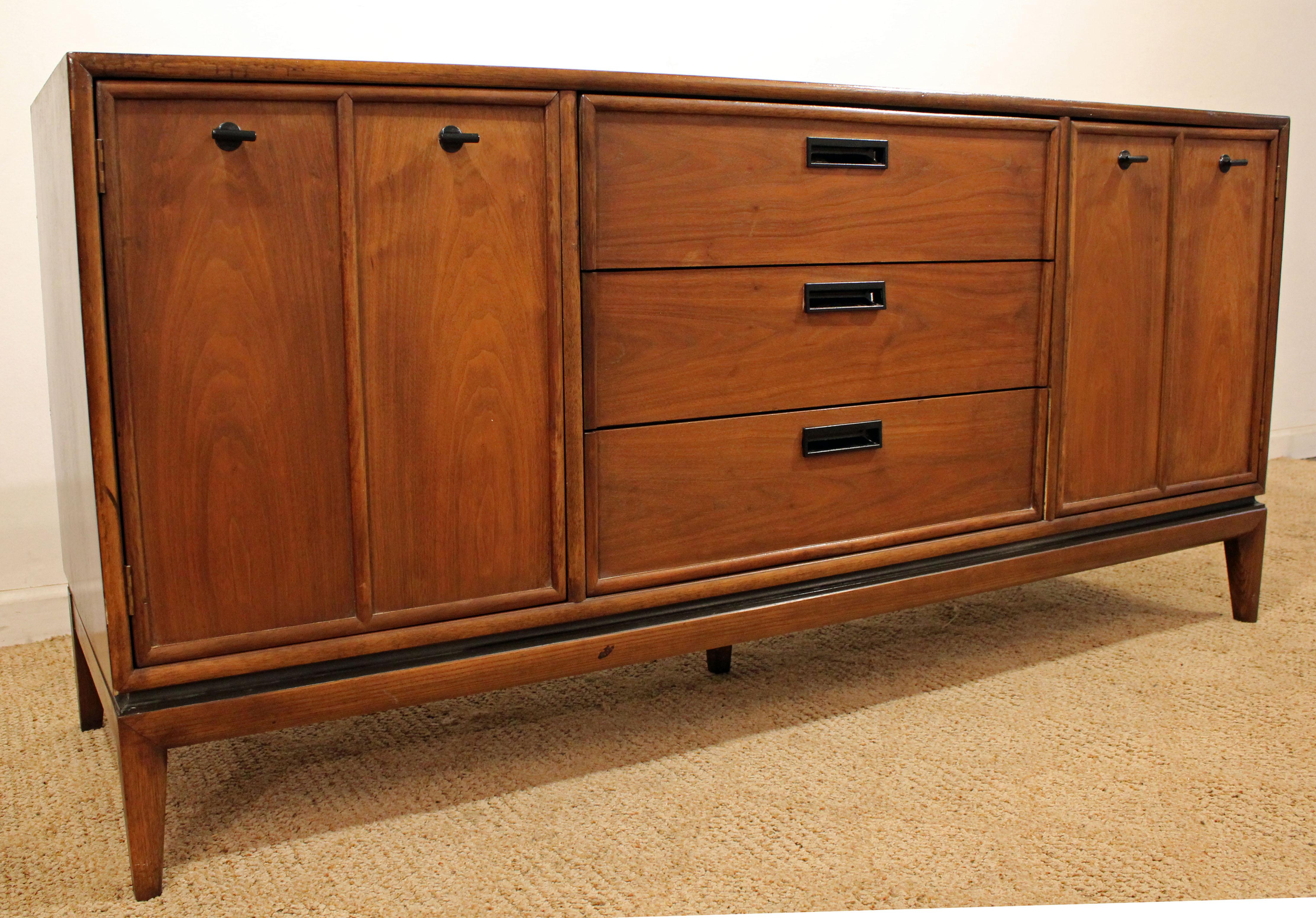 Offered is a Mid-Century Modern credenza. This piece is made of walnut, featuring two doors on each side (with inside shelving on the right side, no shelving on the left) and three centre drawers. The top has been refinished. It is marked by