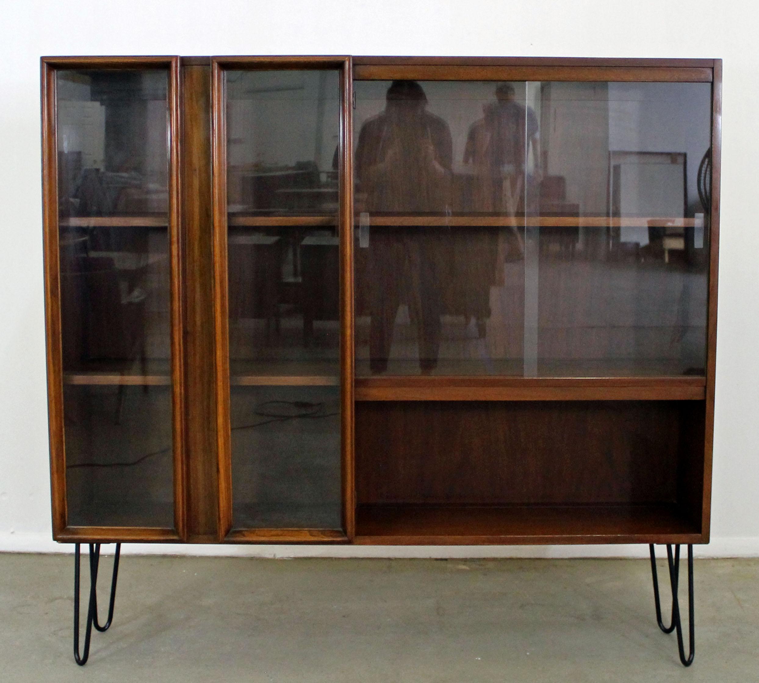 Offered is a piece of time and design; a Mid-Century Modern bookcase on hairpin legs. This piece has been up-cycled from a hutch top to a bookcase with metal 'hairpin' legs. It is made of walnut, featuring glass two glass doors on the right side and