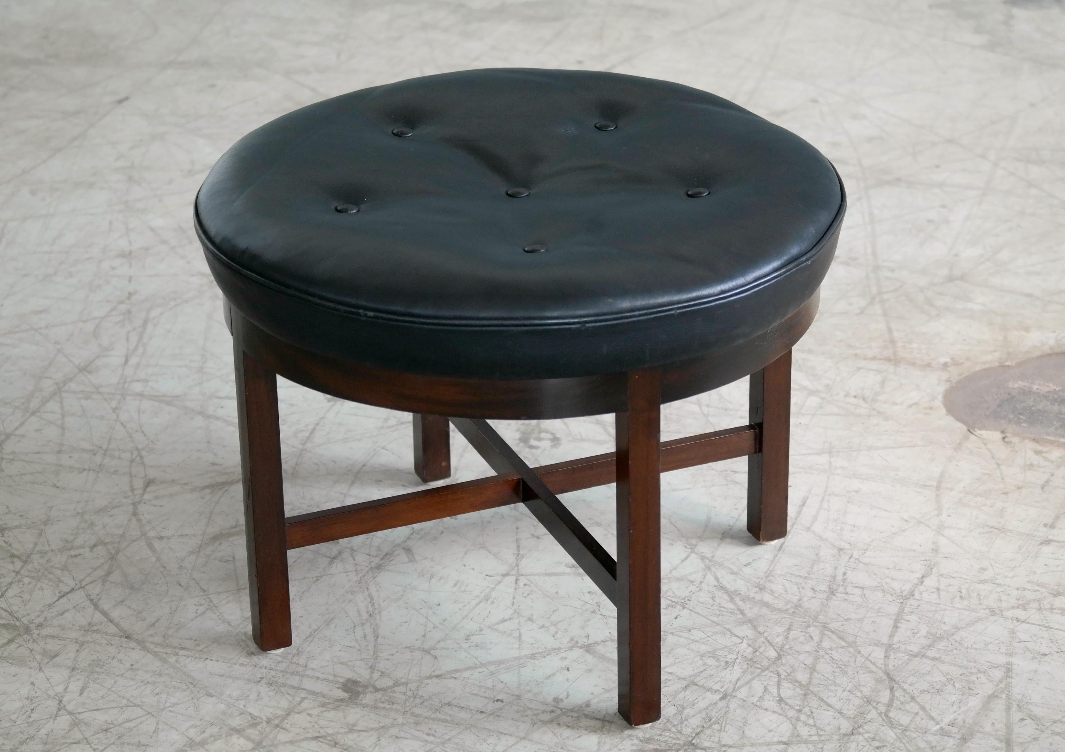 Beautiful 1950s ottoman or footstool from master furniture and cabinet maker Georg Kofoed. Round frame manufactured in mahogany and topped with a handstitched cushion in plush black leather. A great Danish midcentury high-end design that could be