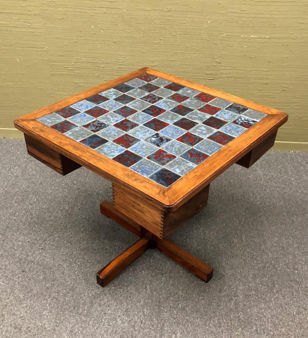 Gorgeous and rare Danish rosewood chess table with blue and cabernet colored inset ceramic tiles by Mogens Lund, circa 1960s. The whimsical original ceramic chess pieces (32 in total) can be stored in four swivel drawers that store under the table.