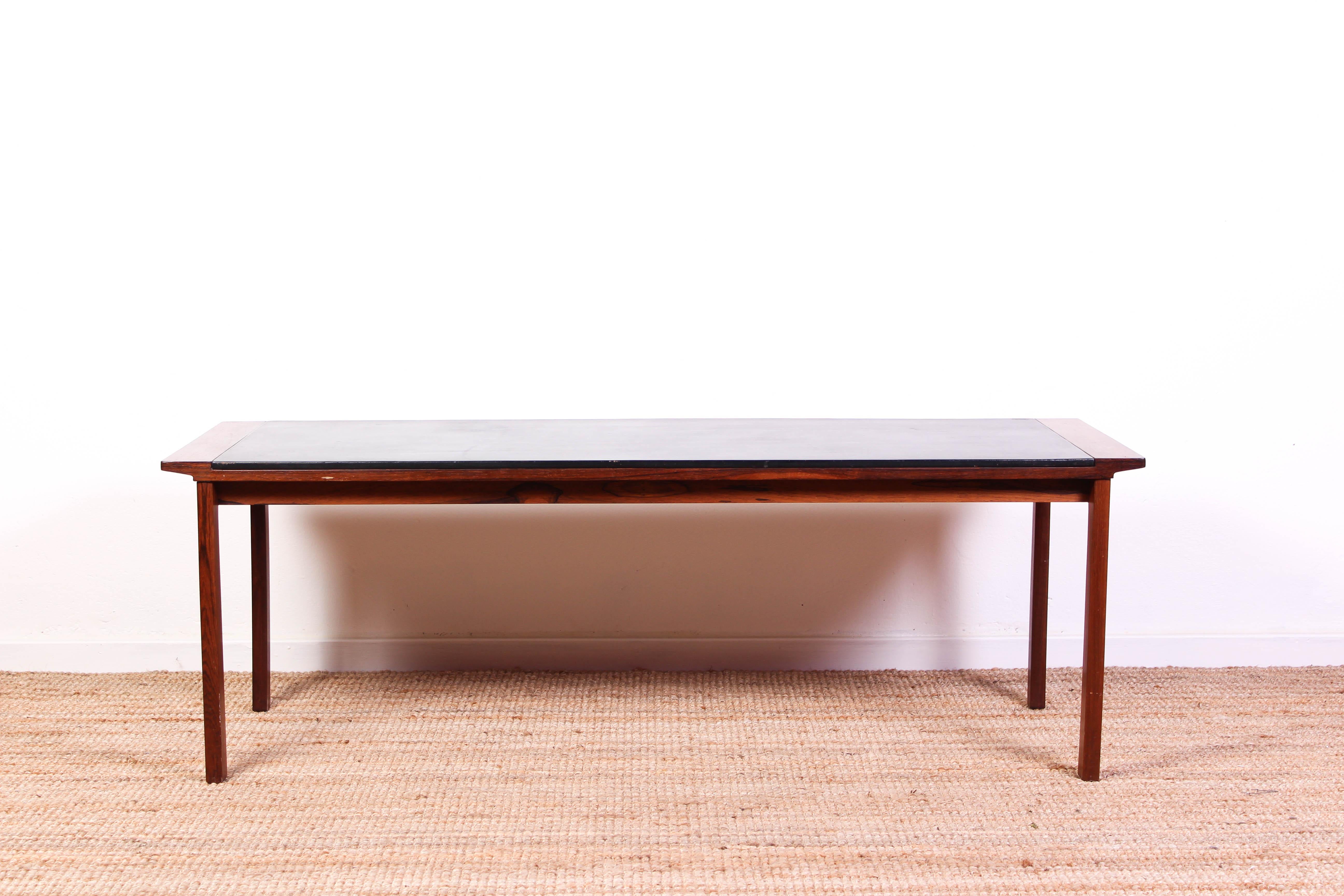 A midcentury Danish coffee table attributed to Ejvind A Johansson. The coffee table is made out of at rosewood frame and a black leather tabletop. It is in very good vintage condition with some signs of usage on the tabletop consistent with age and