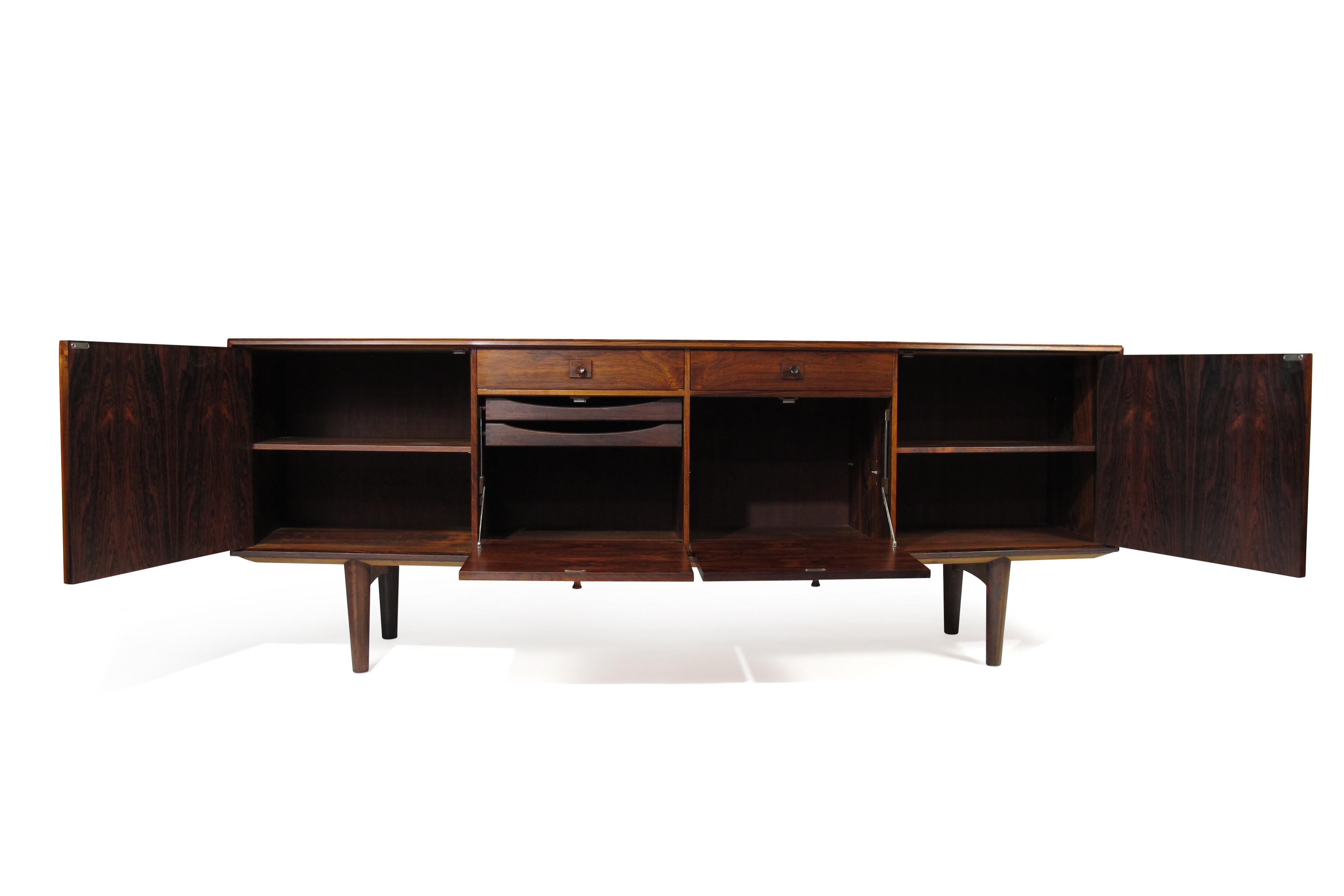 Handcrafted Brazilian rosewood credenza with angled front and bookmatched grain. The sideboard features two doors with adjustable interior shelves, and center section with two drawers over a pair of drop front cabinets with interior silverware