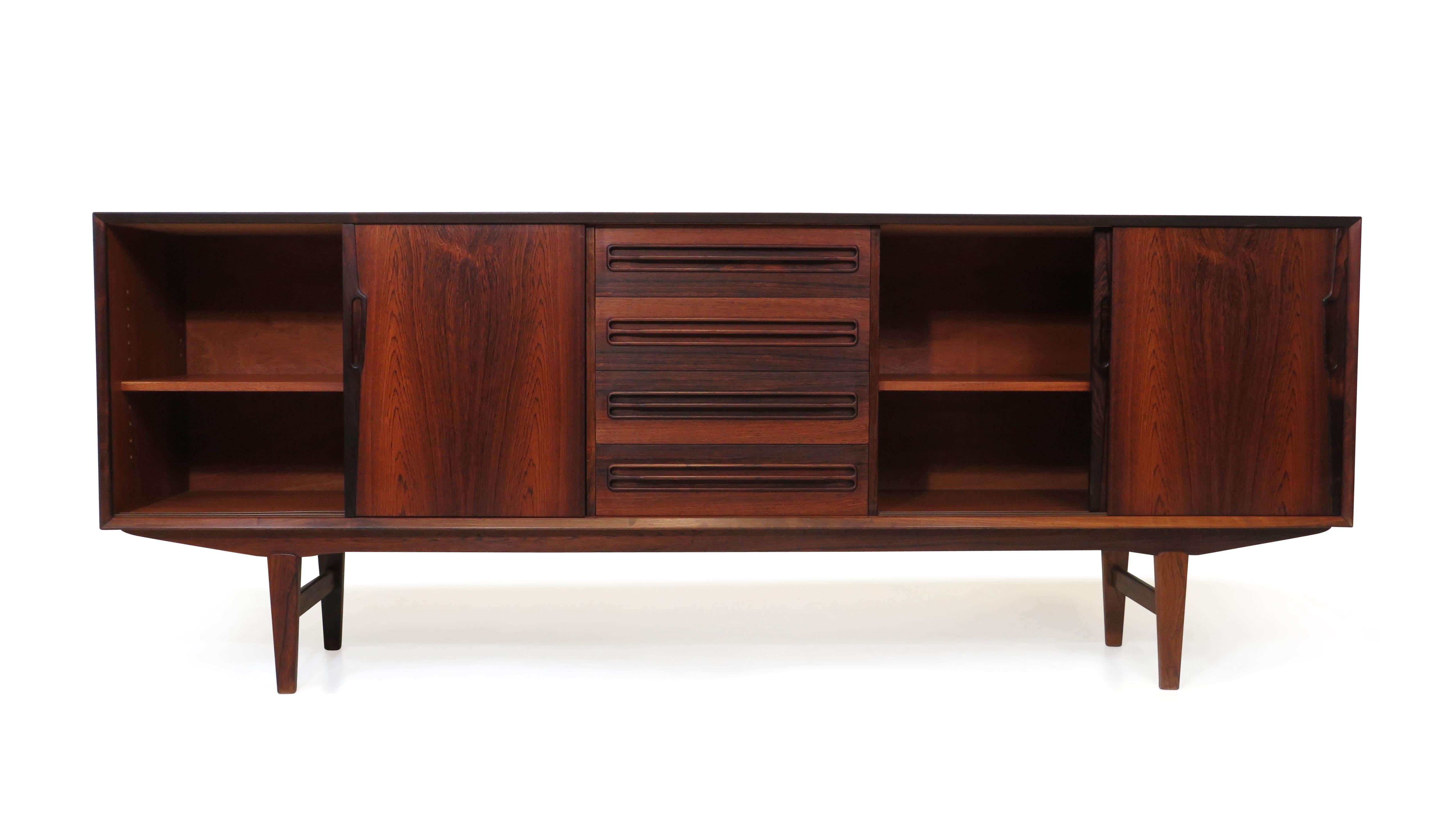 Mid-century Danish Brazilian rosewood credenza finely crafted with mitered edges, book-matched grain and recessed square pulls. The cabinet has four sliding doors revealing a mahogany interior with adjustable shelves and fou drawers in center,