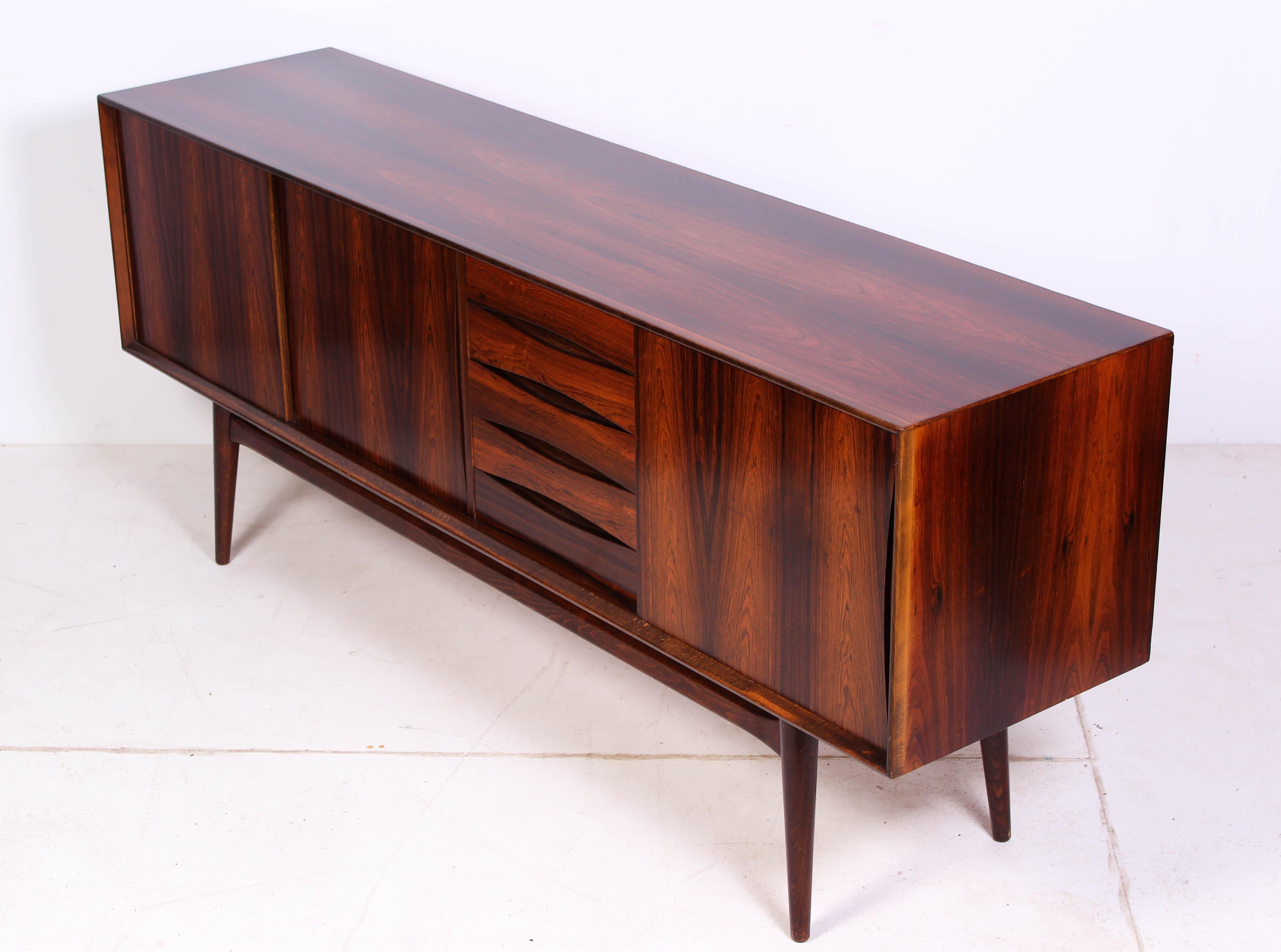 A midcentury rosewood sideboard from the 1950s. The sideboard is elegantly designed with high quality and has nice details such as carved handles in the sliding doors and the drawers. The whole upper part has been professionally refinished and is in