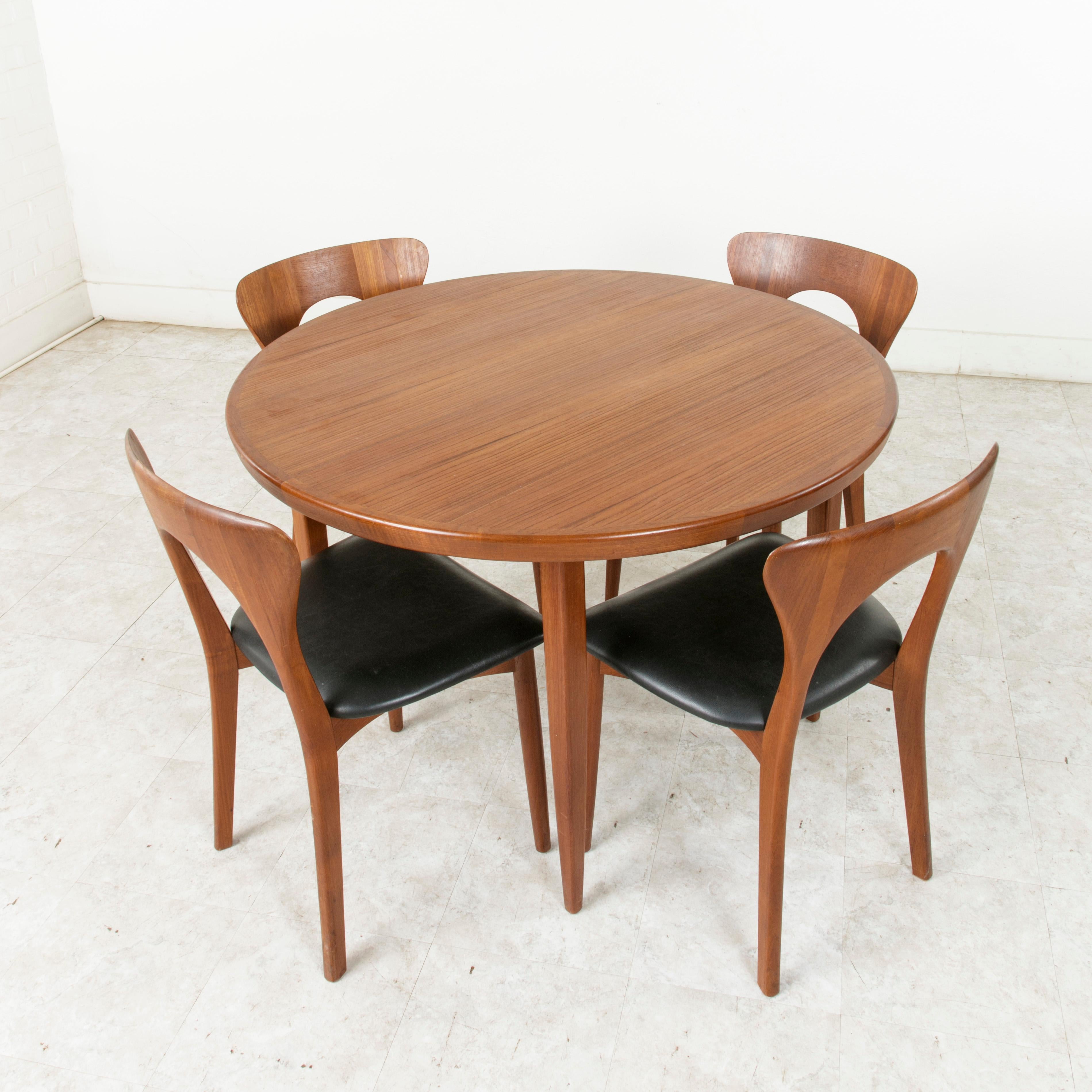 This mid-20th century Danish dining set includes a round teak table and four chairs designed by renowned Danish designer Niels Koefoed. The table measures 43 inches in diameter and rests on slender tapered legs. Its four chairs are of the Peter