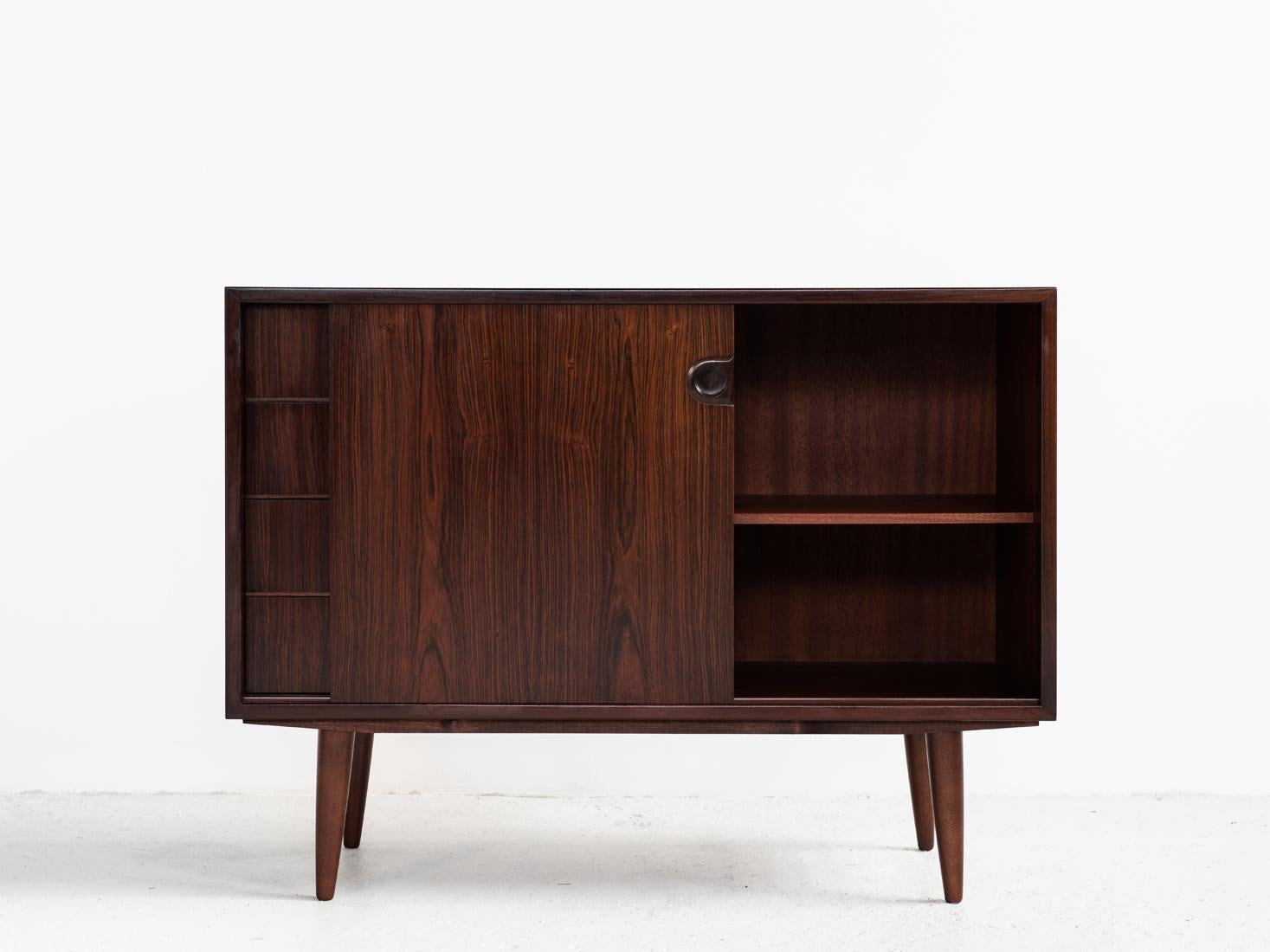 This midcentury sideboard was made in Denmark in the 1960s. We don't know the manufacturer. It shows true high quality manufacturing in rosewood with a beautiful design of the handles. This cupboard has 4 drawers and 1 sliding door. It has round