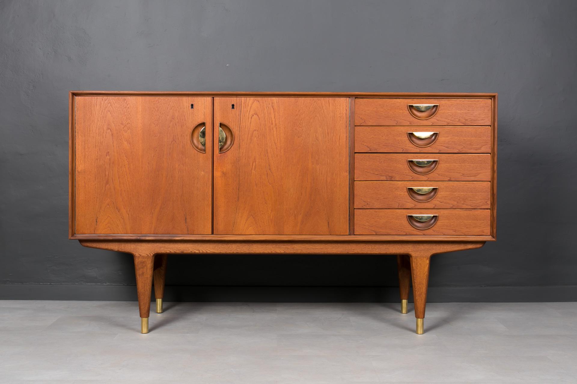 This beautiful teak sideboard was made in Denmark around 1950s. It has one big storage section with height adjustable shelf behind the doors (lockable with a key) and five drawers in the section on the right. The sideboard features beautiful teak
