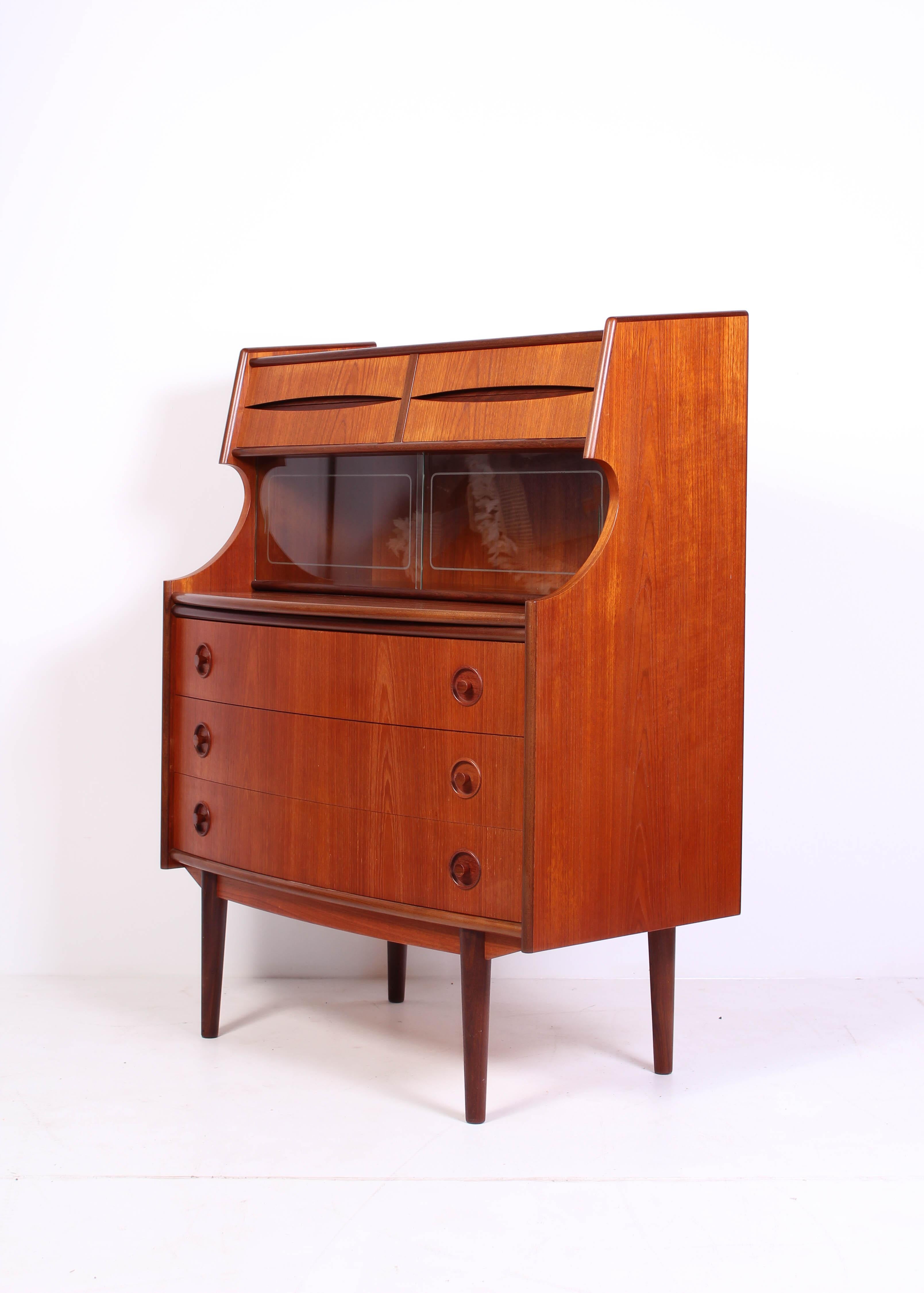 This midcentury Danish teak secretary features a curved front, sliding glass doors and beautiful handles on all drawers. It also features a pull-out leaf so it can be used as a desk. 

This piece is in very good vintage condition with minor signs