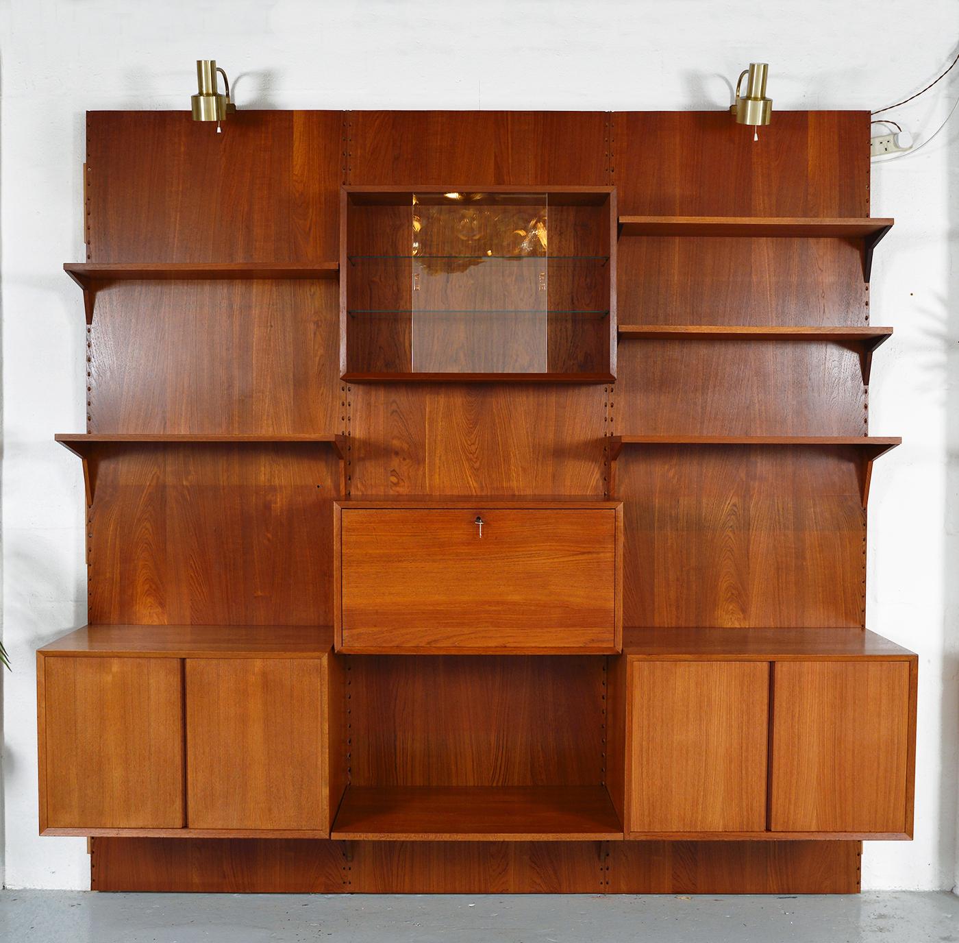 A highly versatile and functional three-bay teak Cado wall system by Danish designer Poul Cadovius. Comprising of three backboards, two cupboards, drop-down bar, glass fronted cabinet, six shelves and brackets - completed by a pair of adjustable