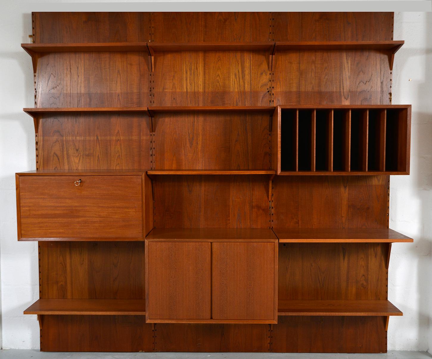 A highly versatile and functional three-bay teak Cado wall system by Danish designer Poul Cadovius. Comprising of three backboards, record cabinet, drop-down melamine bar, two-door cupboard, nine shelves and brackets. 
Wooden dowels fit into the