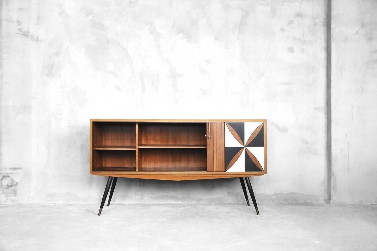 This sideboard was manufactured in Denmark during the 1950s. It is made of solid wood and teak veneer. The piece features two hidden tambour doors with handles and automatic locks, adjustable interior shelves, turned legs with brass feet, and the
