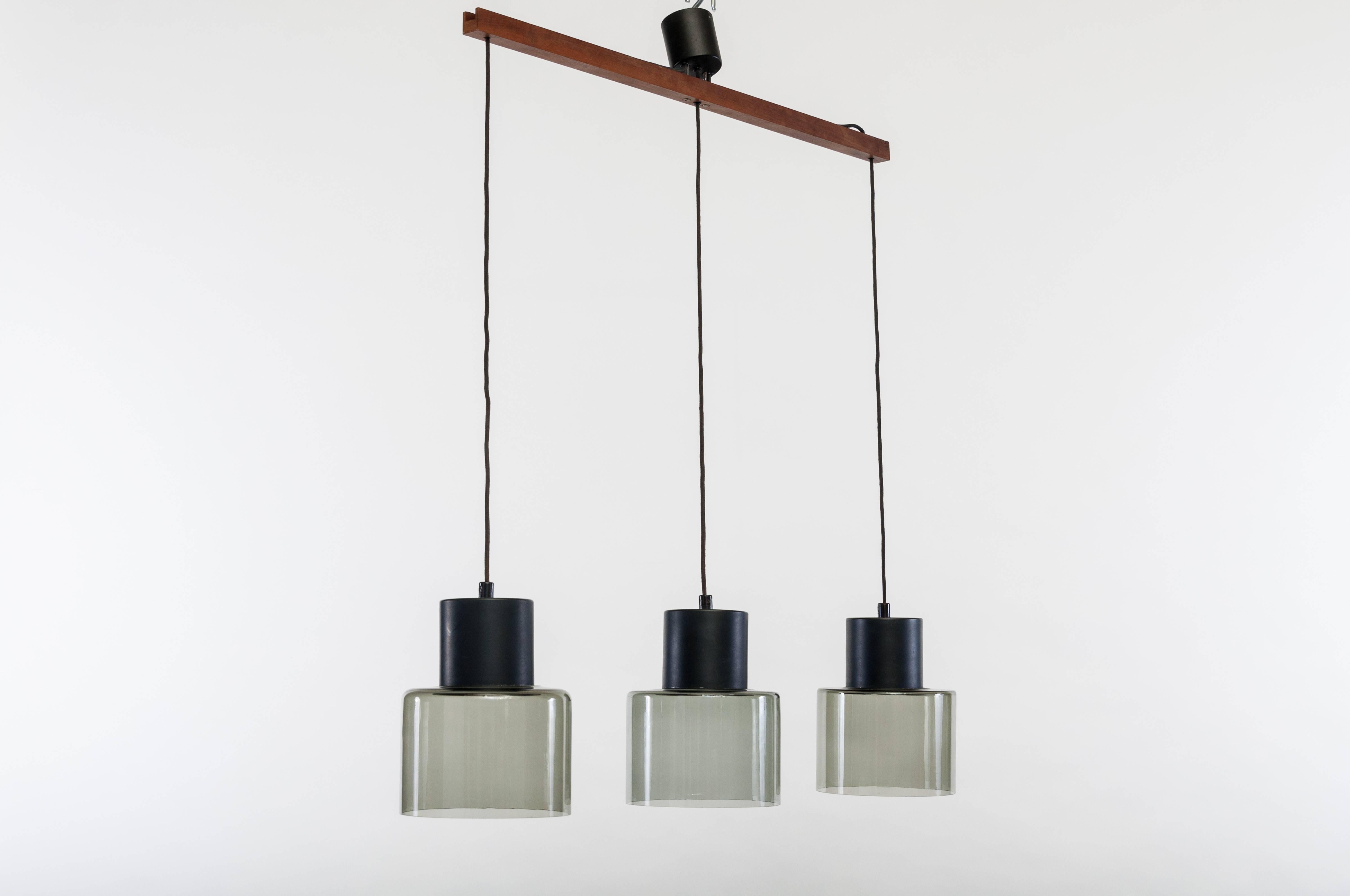 Scandinavian chandelier designed by Tapio Wirkkala and produced by the Finnish manufacturer Idman during the 1950s. 
The light features a wood ceiling mount, a black lacquered metal frame, and three smoked glass pendant lights. 
The lamp is signed