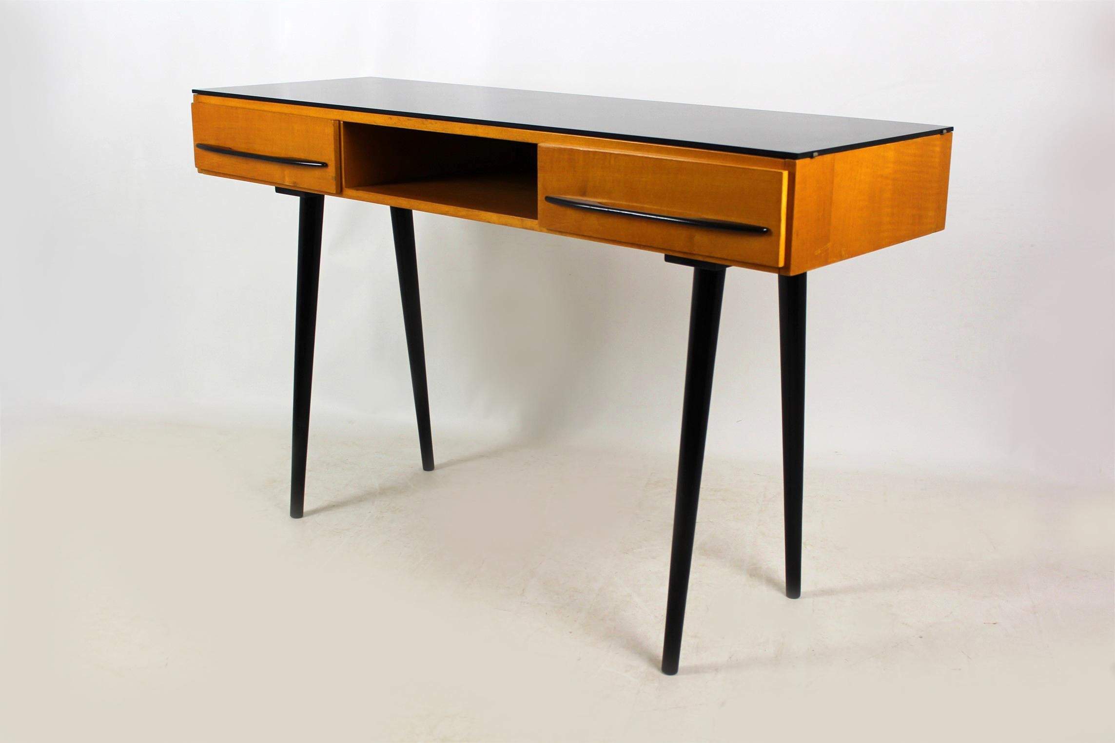 Midcentury small desk which can also be used as a console table. Designed by Mojmír Požár in 1957 and manufactured by UP Bucovice in former Czechoslovakia during the 1960s. Features two drawers, retains its original black glass on the top. Woodwork
