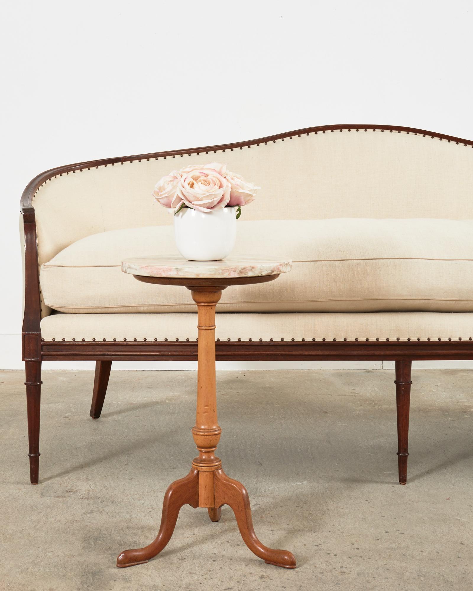 Handsome 19th century English Georgian mahogany tripod drink table or candle stand featuring a variegated marble top. Crafted from mahogany with an aged faded patina. The round top is supported by a turned column pedestal ending with tripod legs.