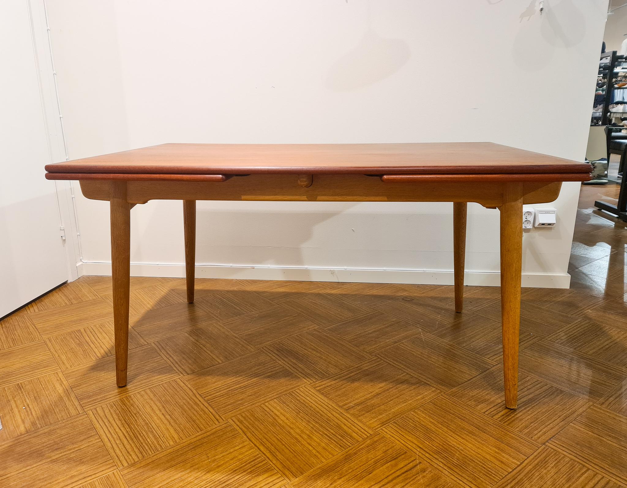Wonderful dining table produced by Andreas Tuck and designed by Hans J Wegner in the 1950s.

The dining table has a frame of solid oak and a top of teak veneer. Two pull-out-leaves make extension possible. The two leaves hide under the top and is