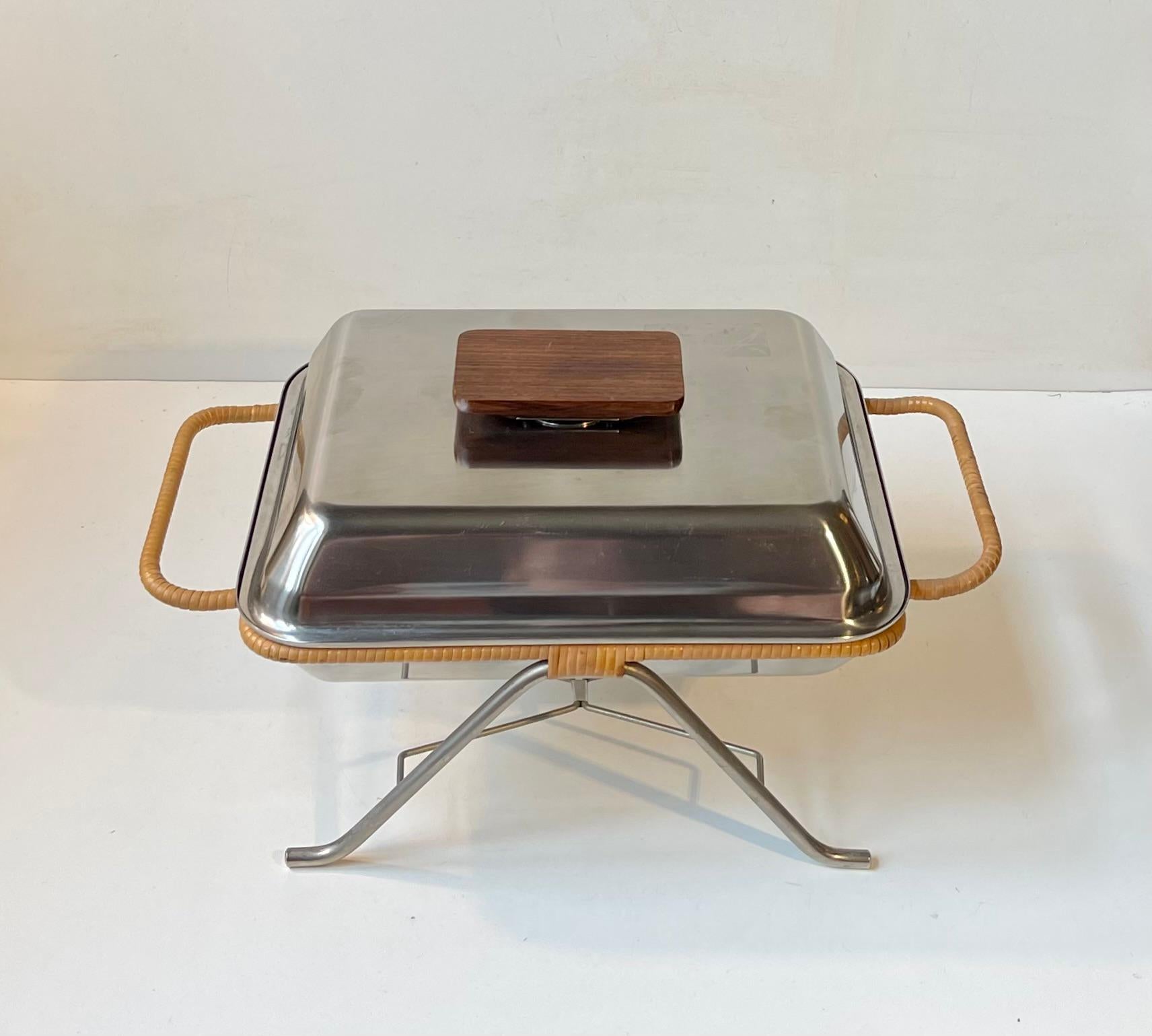 A very rare domed dinner serving tray or cloche in brushed stainless steel and a jumbo handle in solid teak. The holder/base is also fashioned from stainless steel and it features twisted rattan around its sides and handles. The center of the base